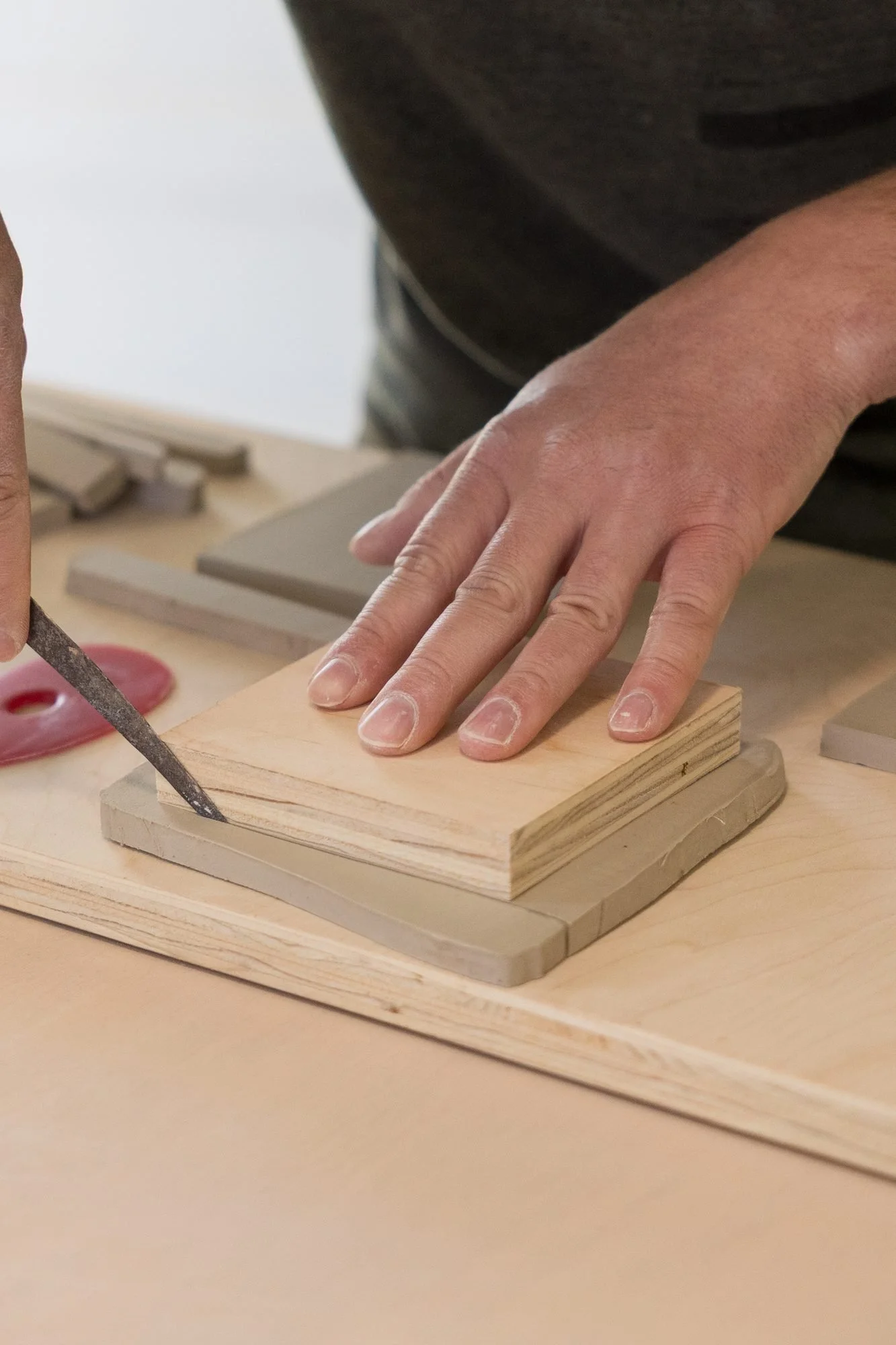 A hand pressing down on a stack of clay slabs while another hand holds a knife
