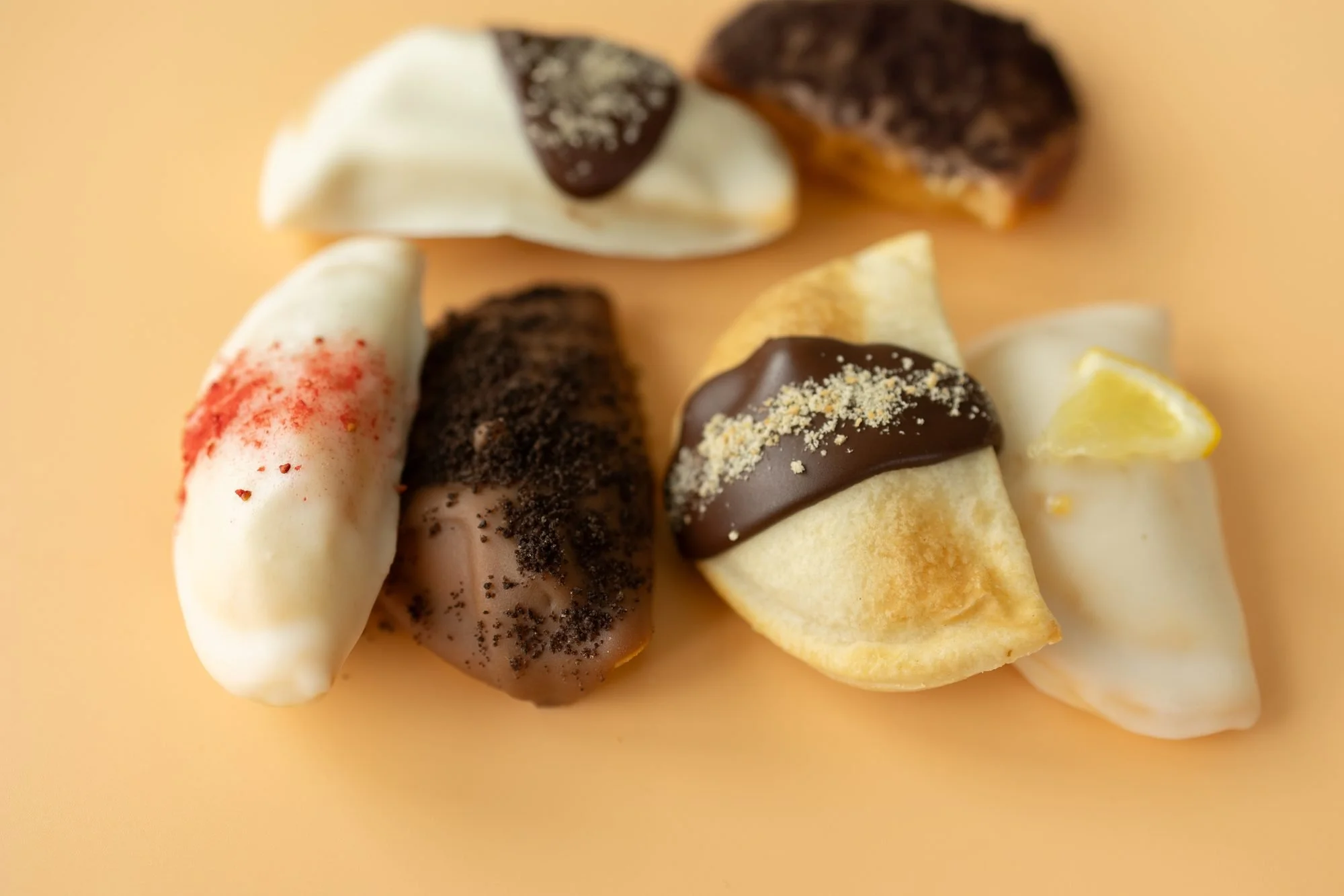 Assorted glazed and chocolate dipped hand pies arranged on a peach background