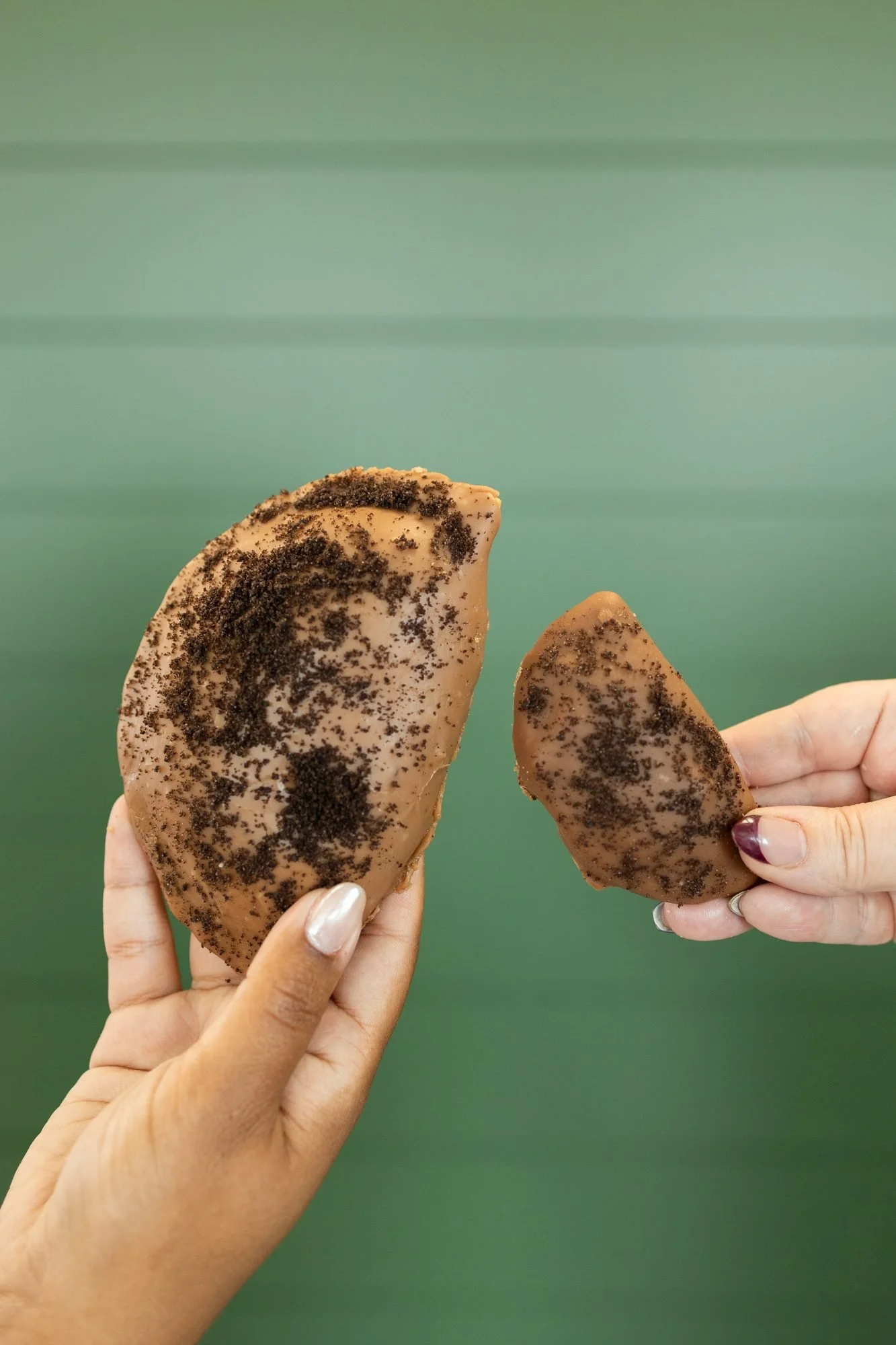 Two hands holding chocolate crumble hand pies, one broken open, in front of a green wall