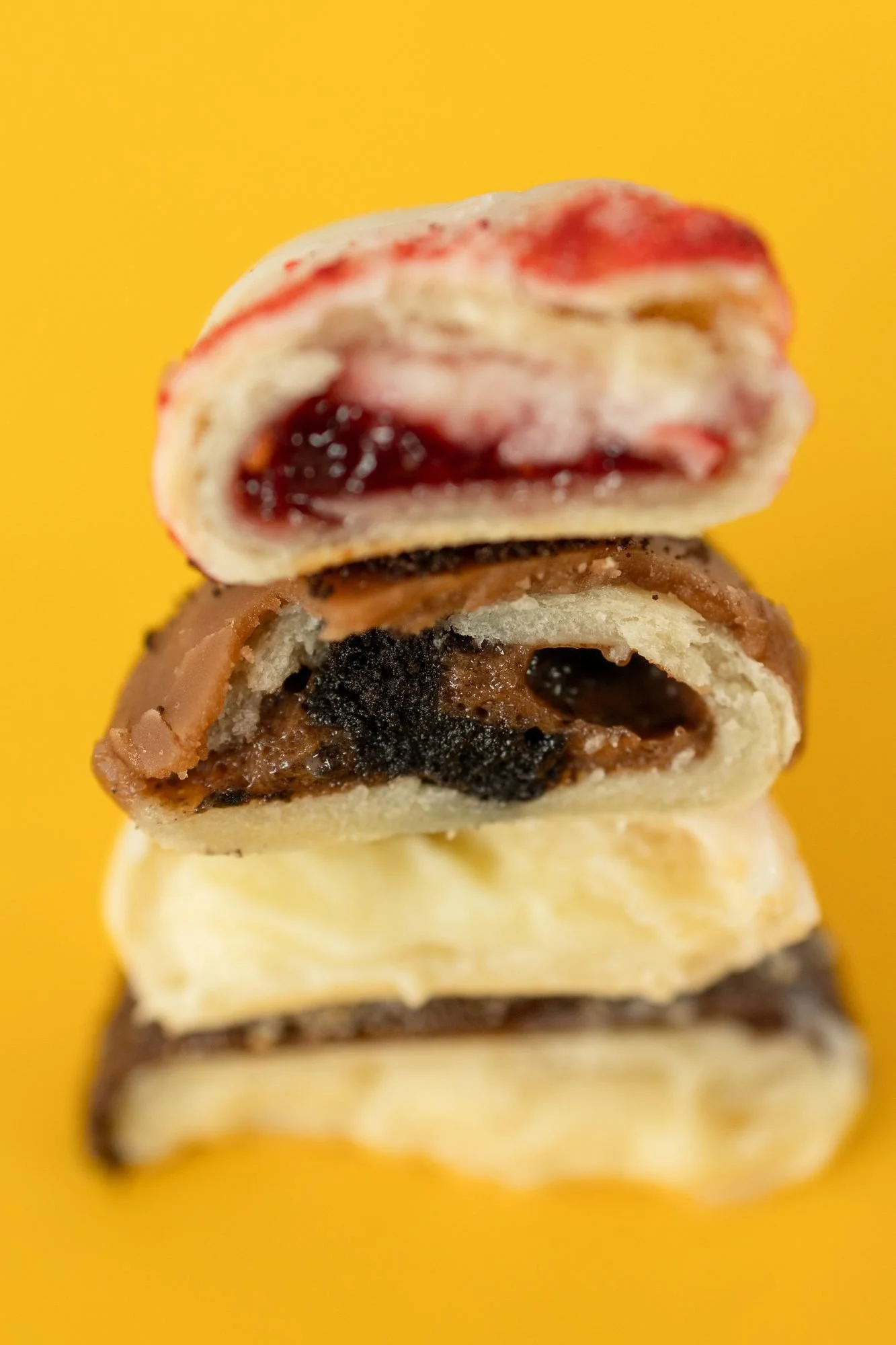Three hand pies stacked and cut in half showing jam, chocolate and cream fillings on a yellow background