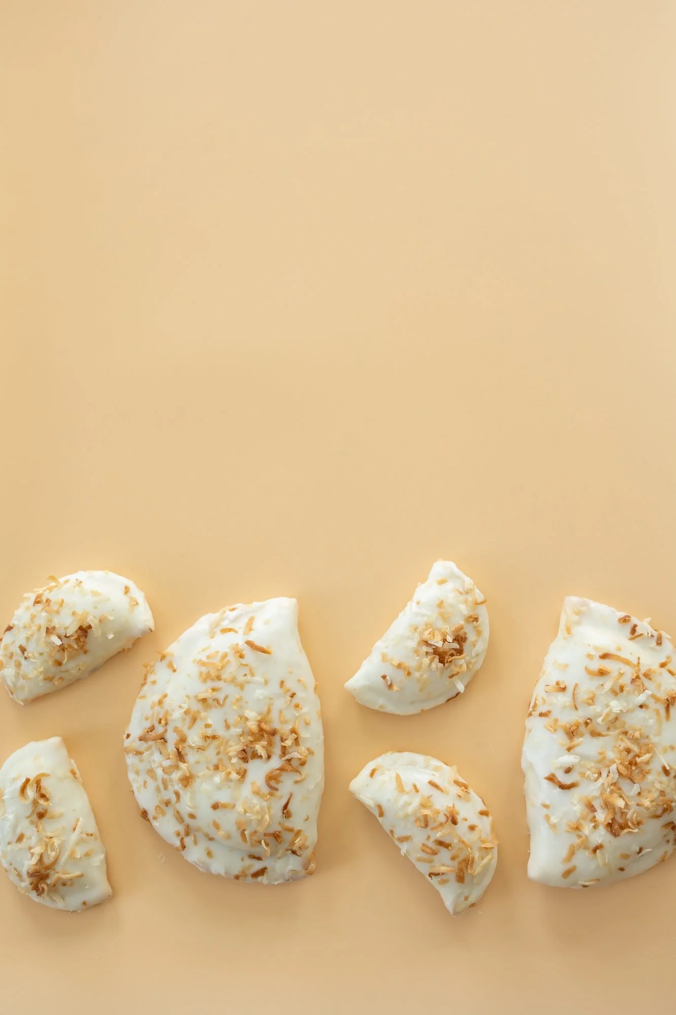 Several coconut topped white glazed hand pies arranged on a peach background
