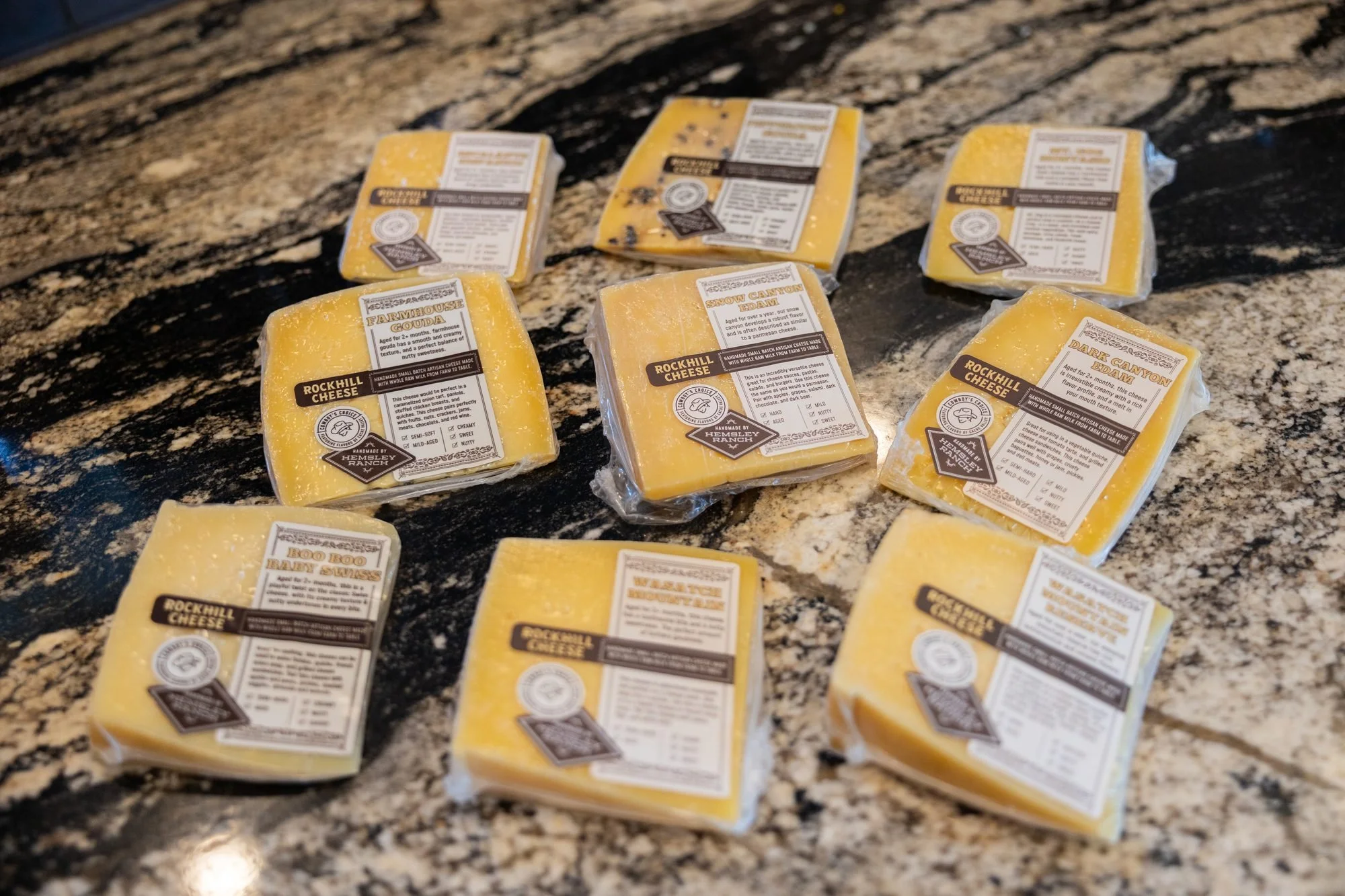 Several wrapped wedges of Rockhill Cheese laid out on a dark speckled stone counter