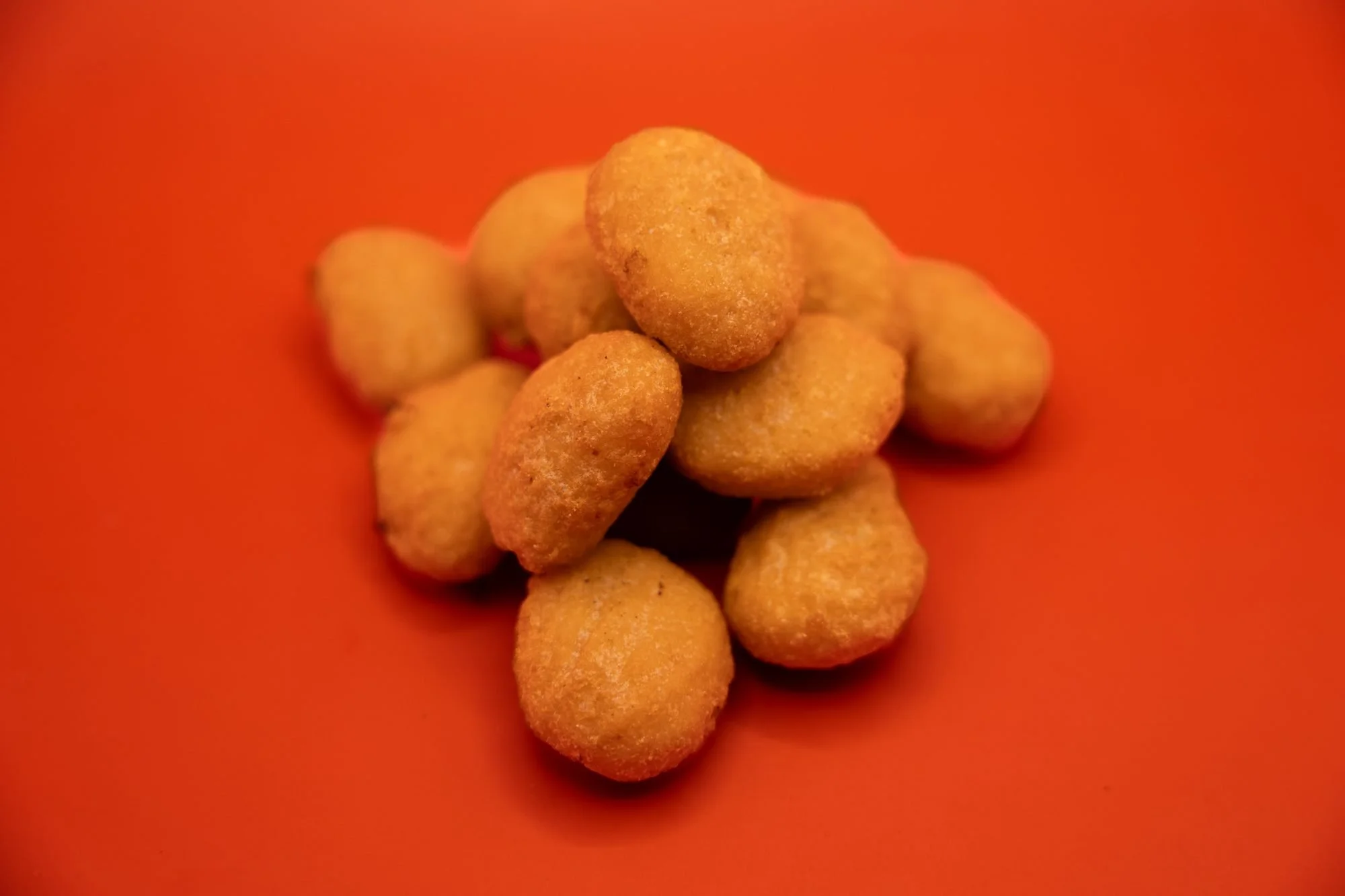 A pile of golden fried cheese curds on a bright orange background