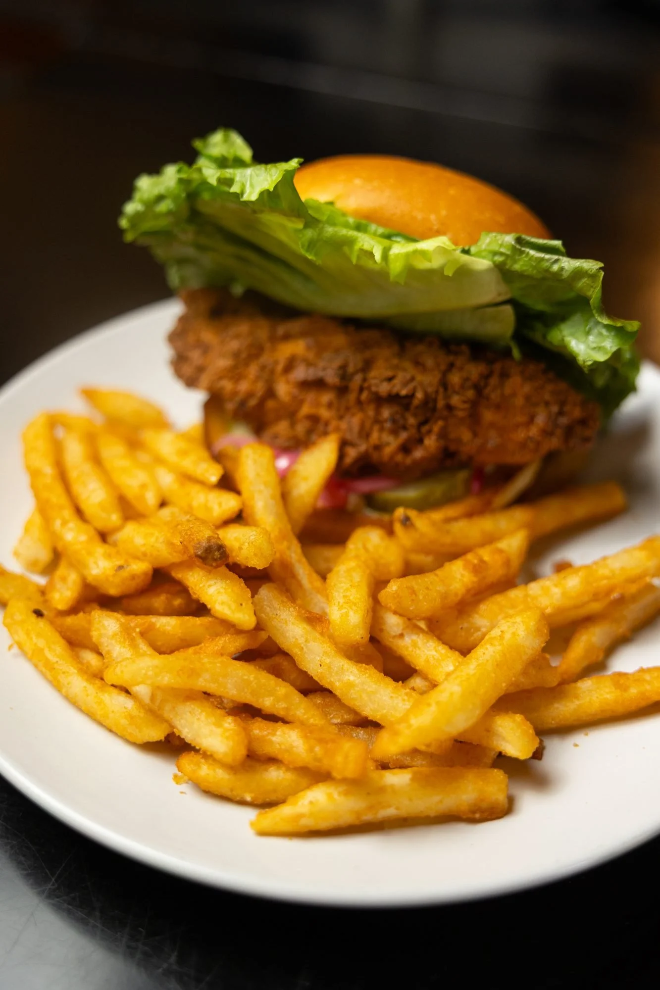A crispy chicken sandwich with lettuce beside a pile of seasoned fries on a white plate