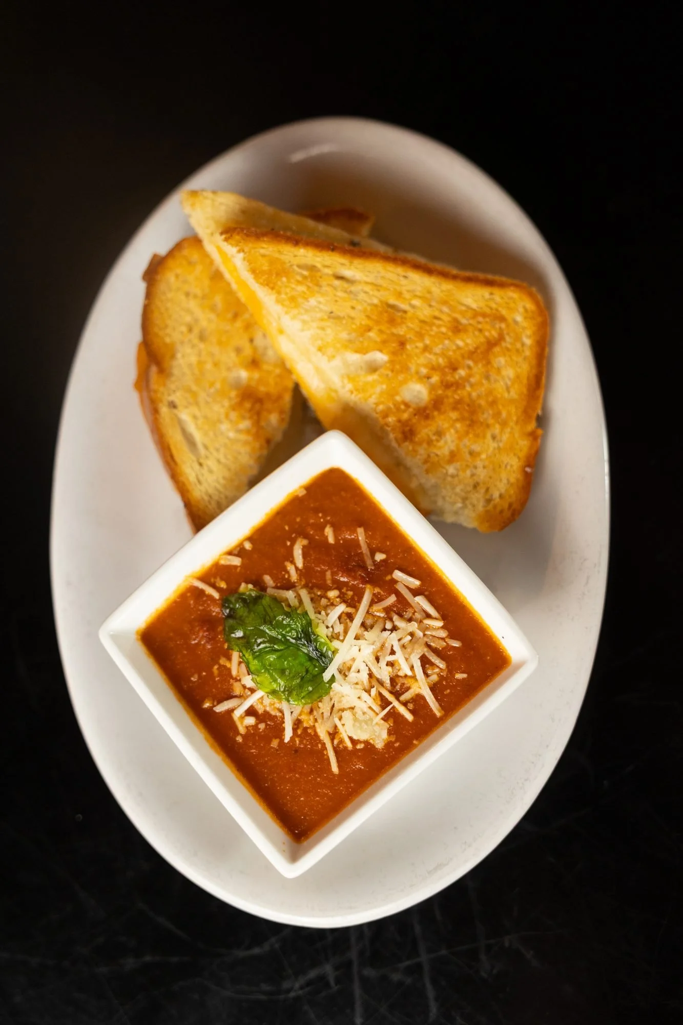 A grilled cheese sandwich cut in triangles with a bowl of tomato soup on an oval white plate