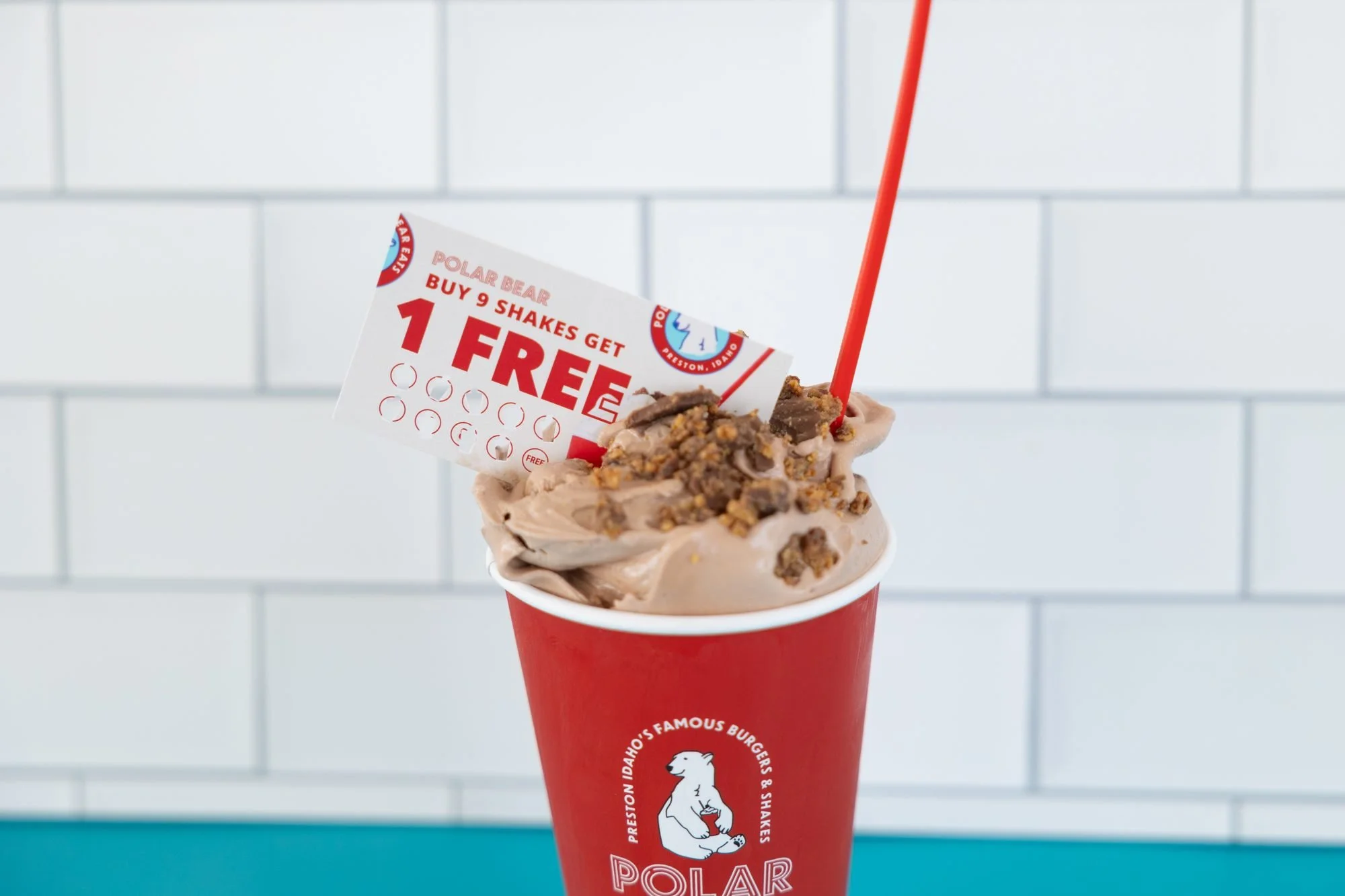 A red Polar Bear cup of chocolate soft serve with candy pieces and a punch card, set on a teal counter against white tile