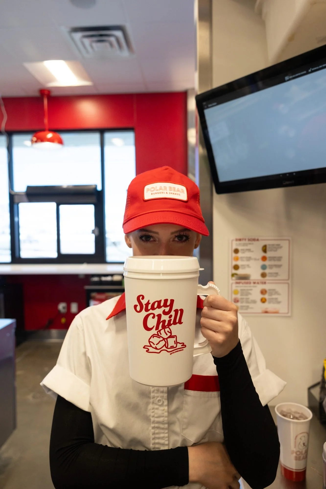 A Polar Bear employee holds a Stay Chill mug inside the restaurant near a menu screen