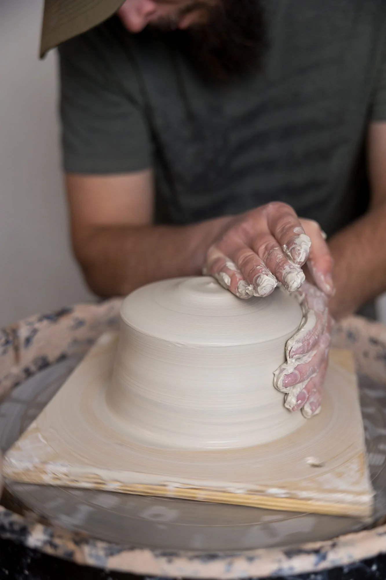 A potter cups his hands around a flattened mound of clay on a wheel, seen from above