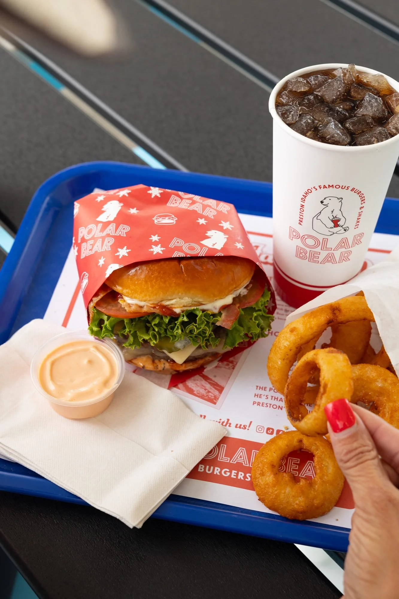 A hand reaches for onion rings beside a burger and drink on a blue tray