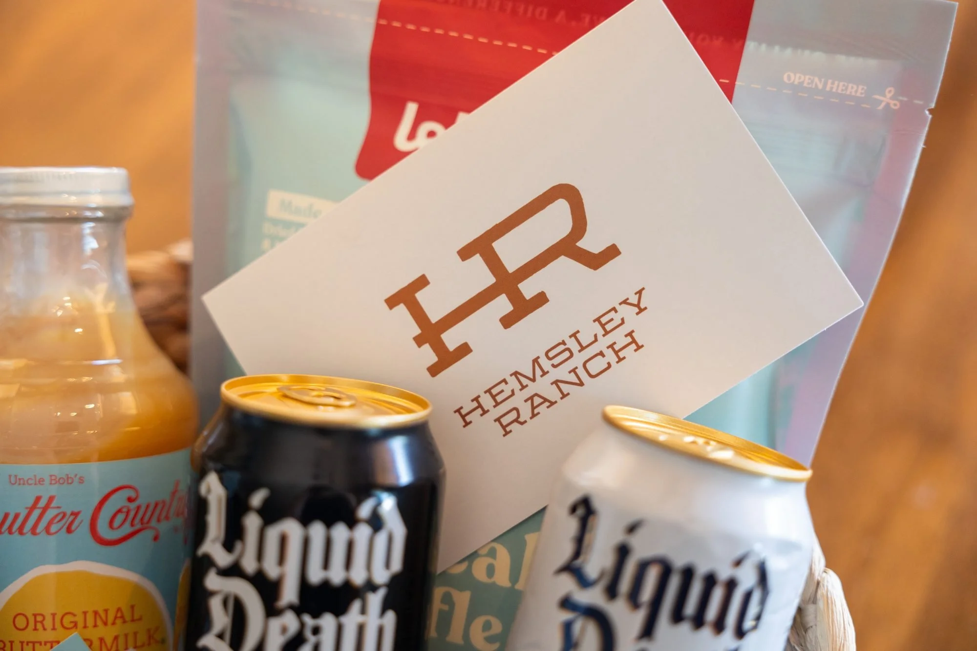 A Hemsley Ranch card propped among canned waters, a juice bottle and a bag in a gift basket