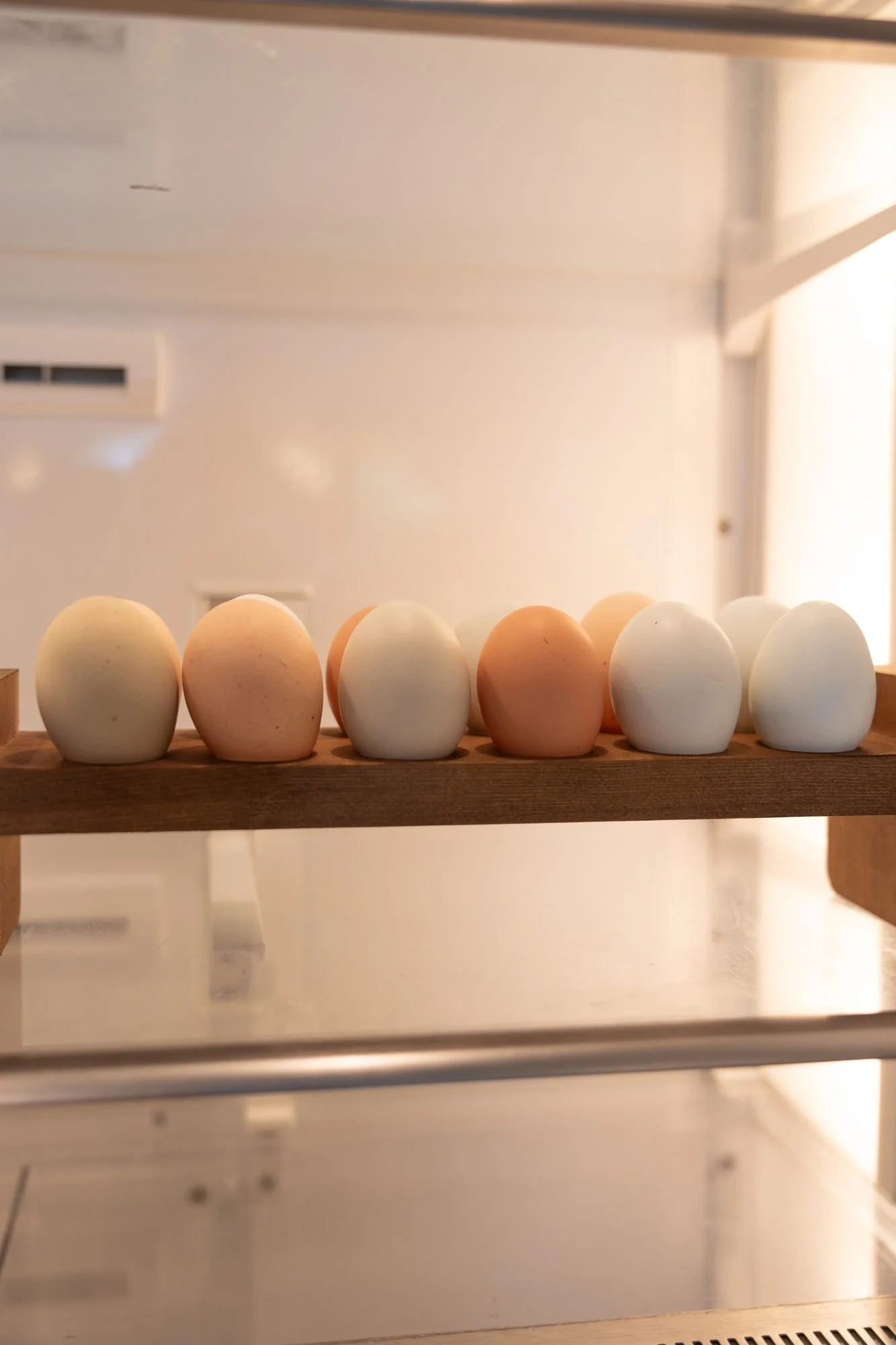 A row of brown, white and blue eggs sits on a wooden rack inside a clean white display case
