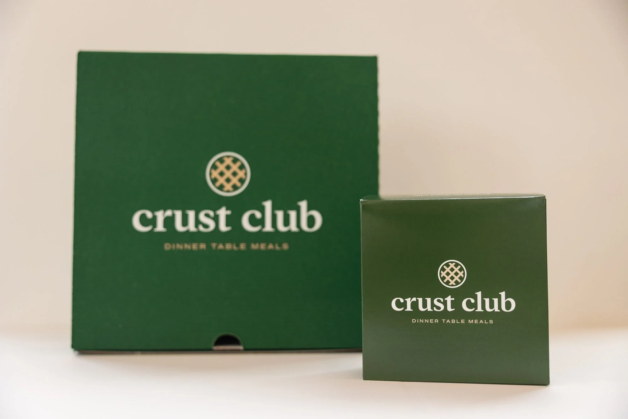 Two green Crust Club boxes standing upright on a white surface