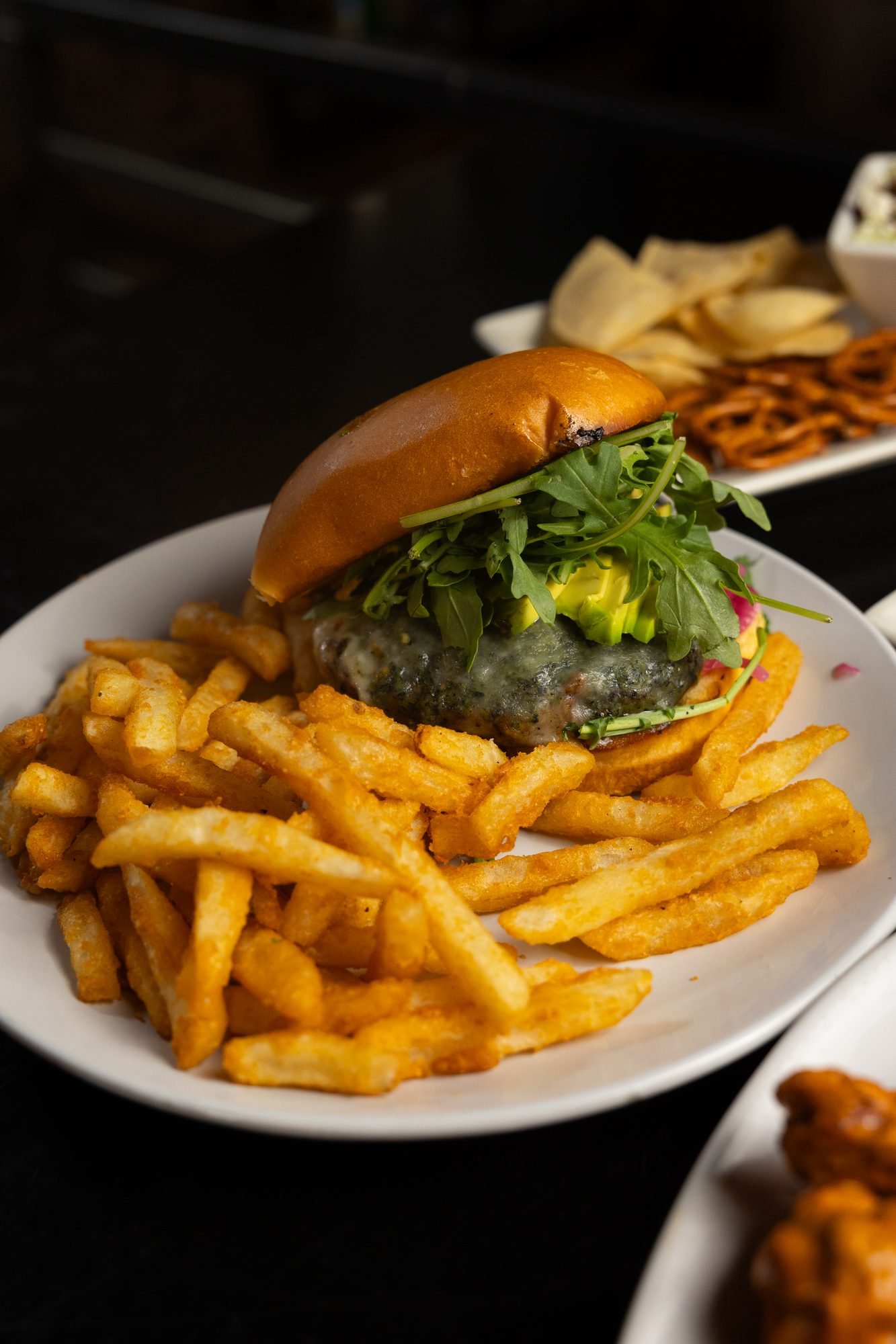A burger with greens on a brioche bun beside a pile of seasoned fries on a white plate