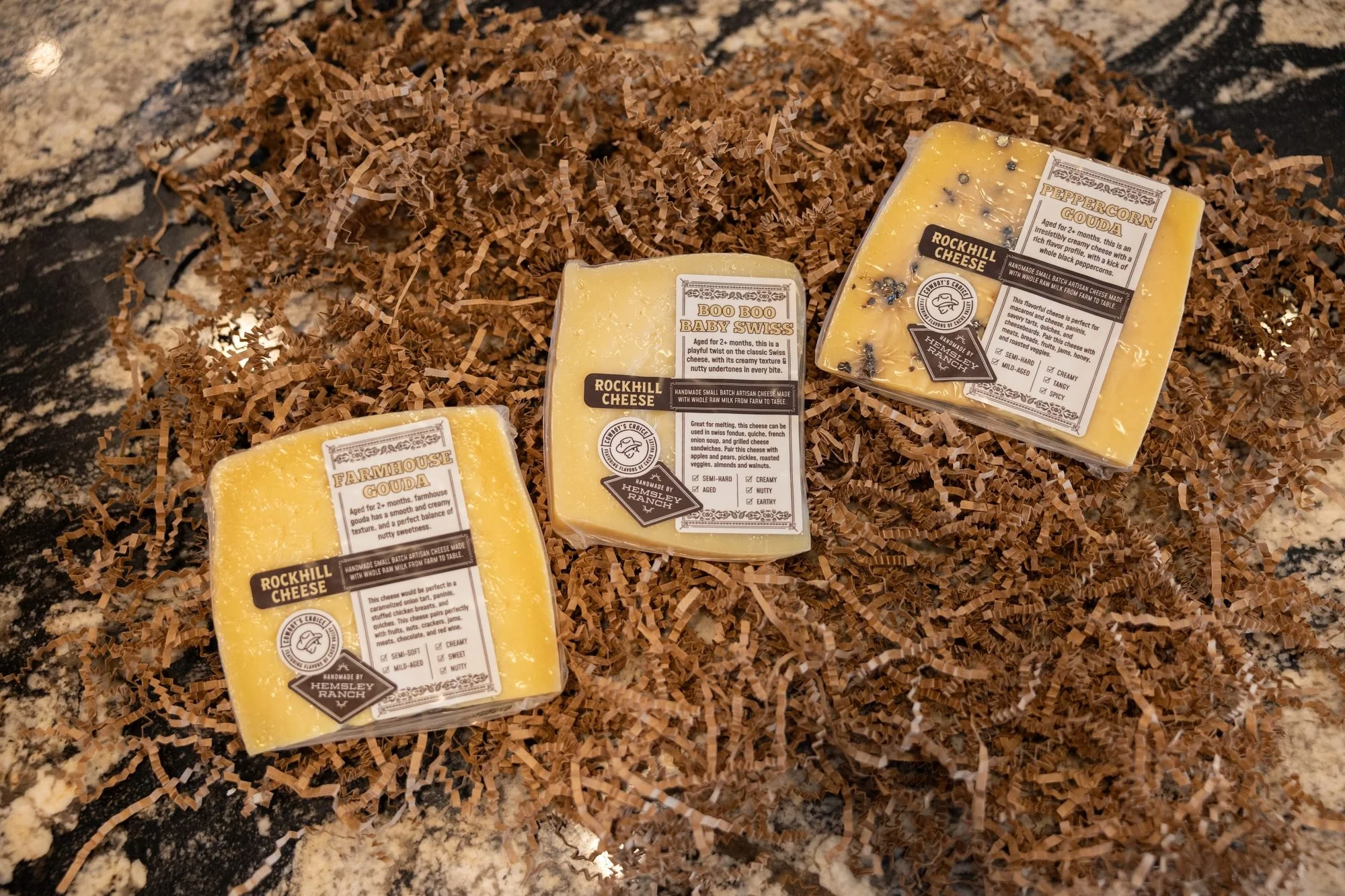 Three wrapped wedges of Rockhill cheese rest on brown paper shred on a granite counter