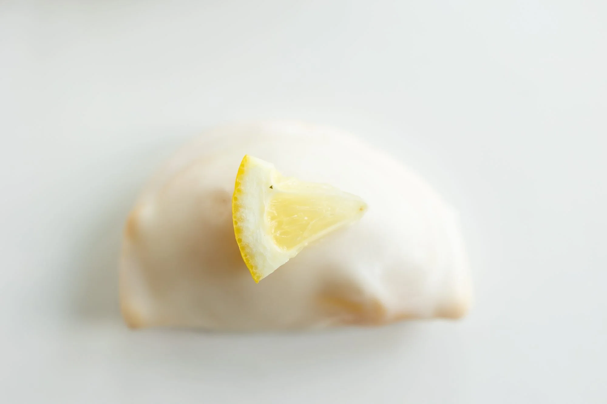 A glazed hand pie with a lemon wedge, shot low on white