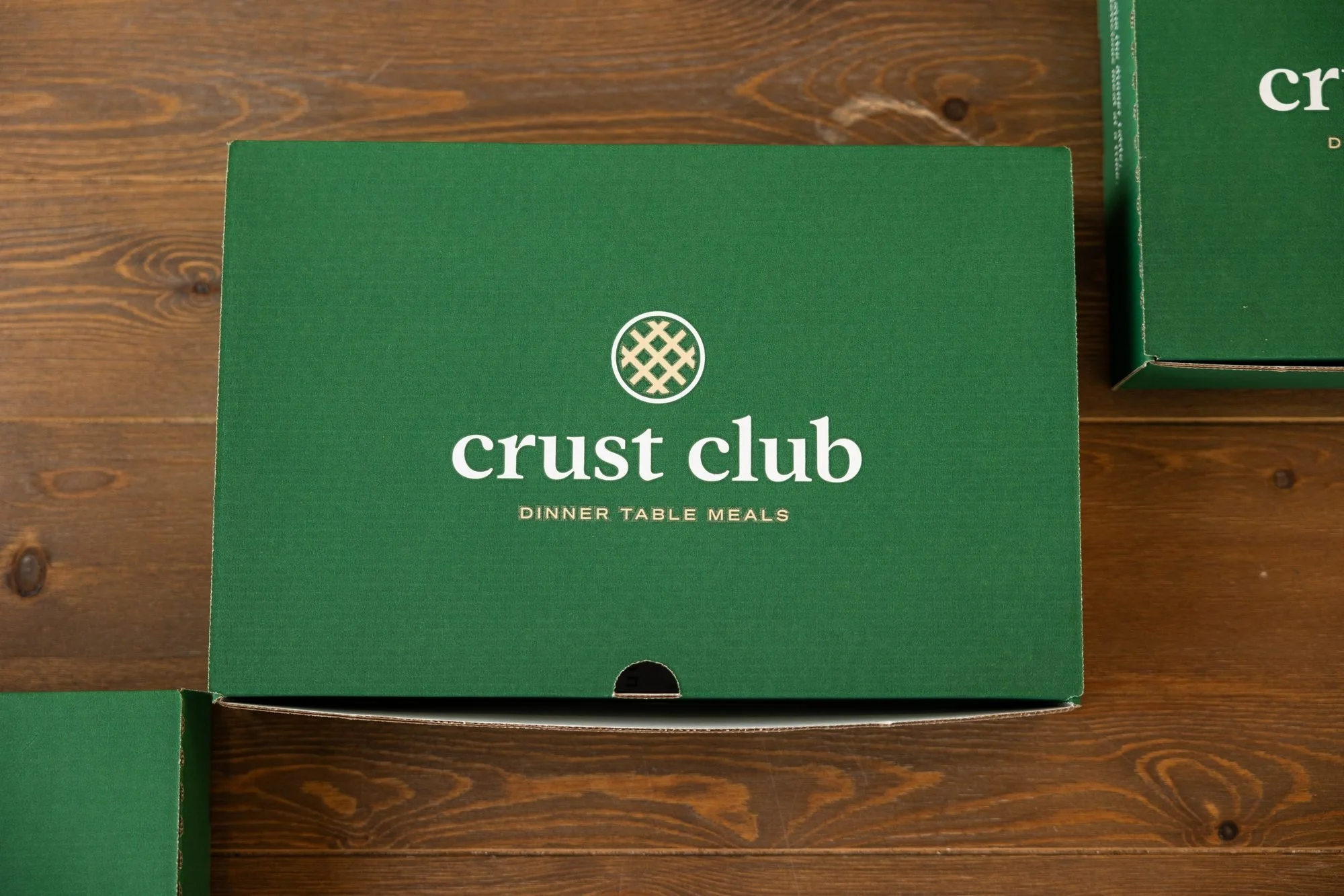 A green Crust Club box sits on a dark wood table with more boxes beside it