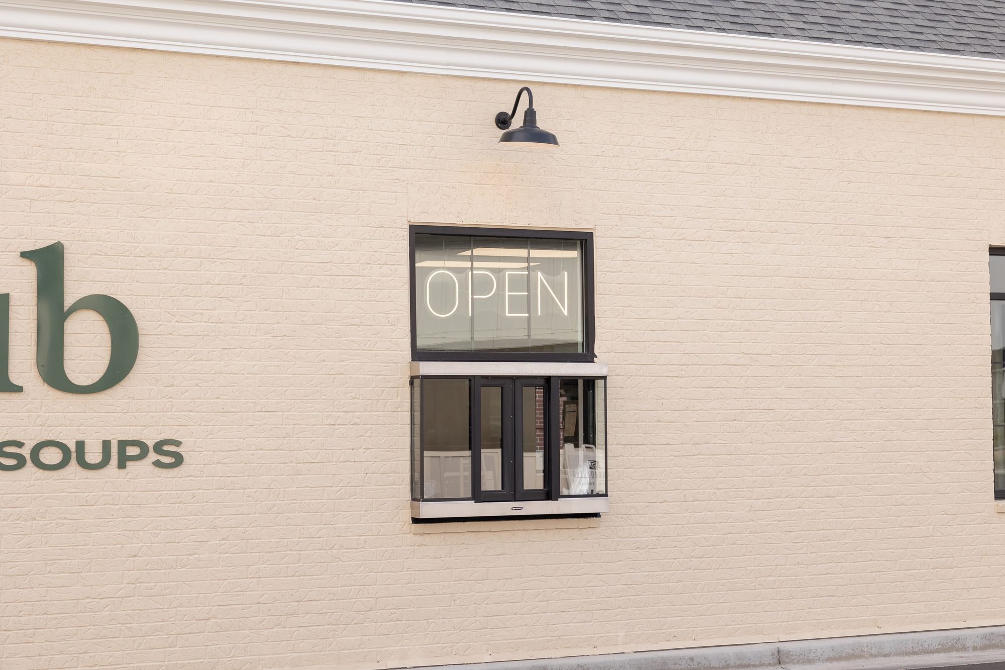A cream brick wall with a Crust Club sign, a wall lamp and a window with a neon OPEN sign