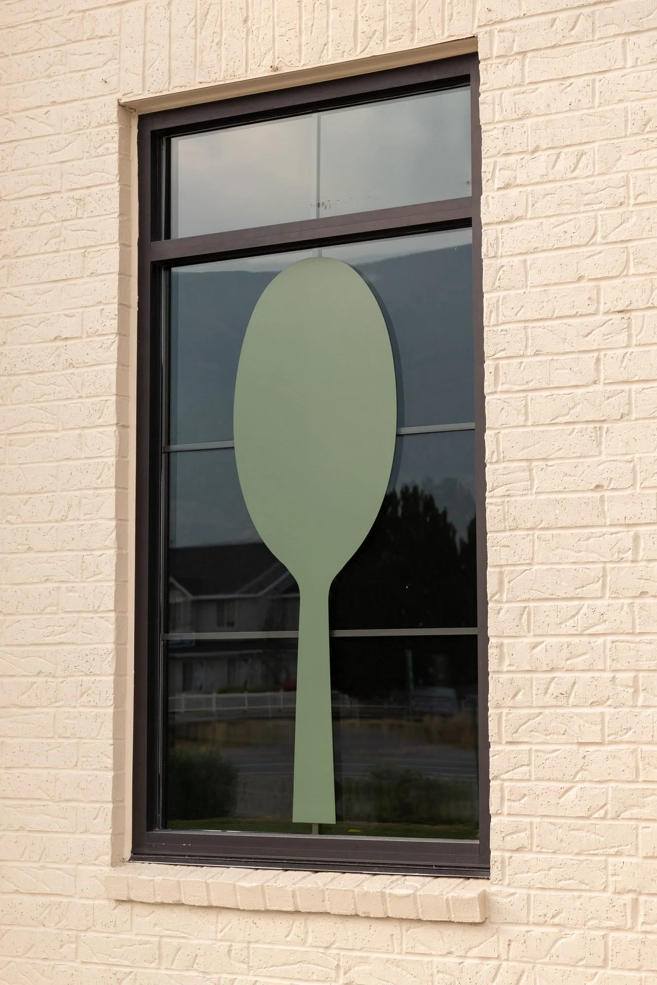 A tall window on a cream brick wall with a large green spoon graphic