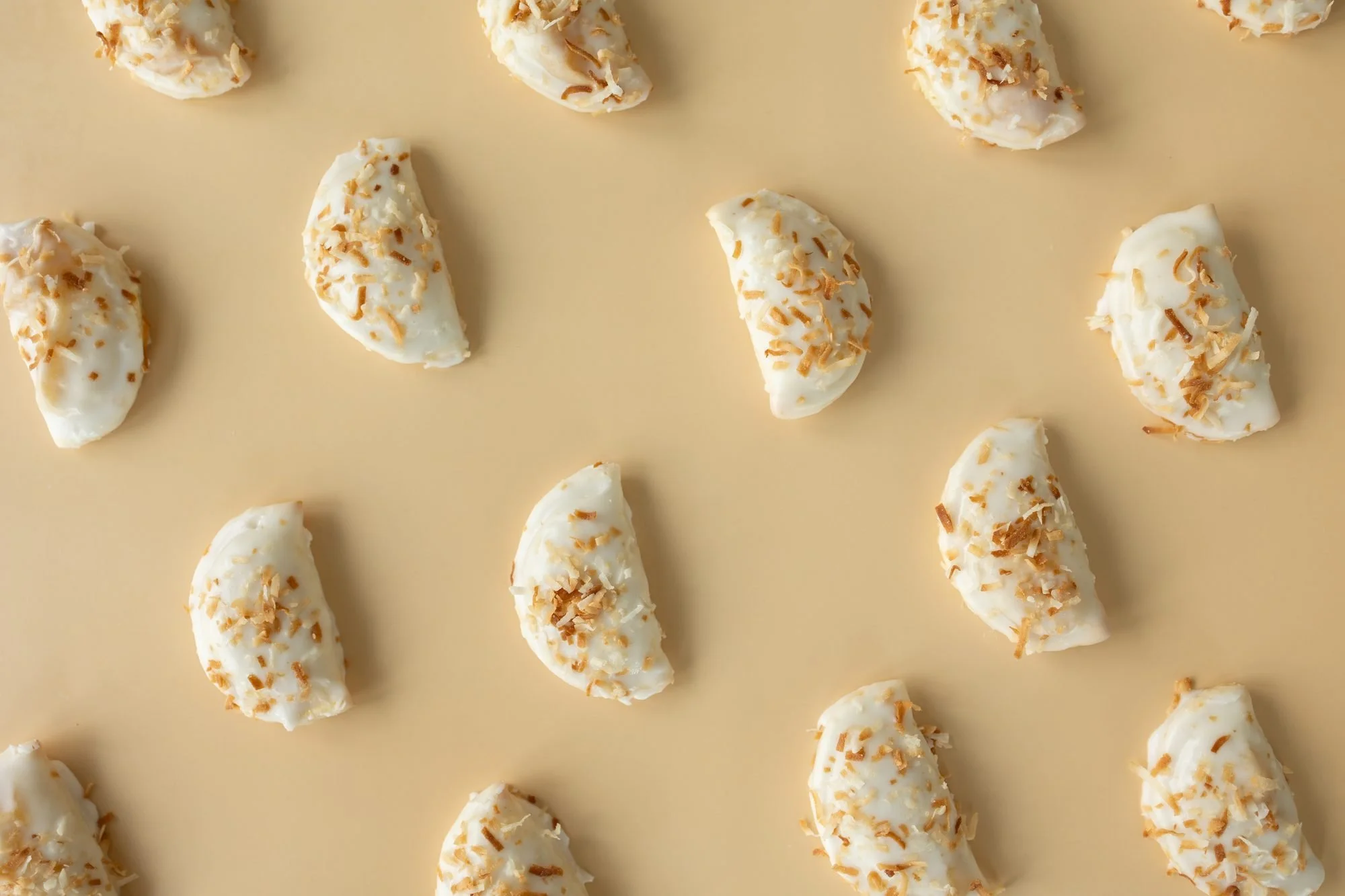 Rows of white-glazed hand pies topped with toasted coconut arranged on a tan background