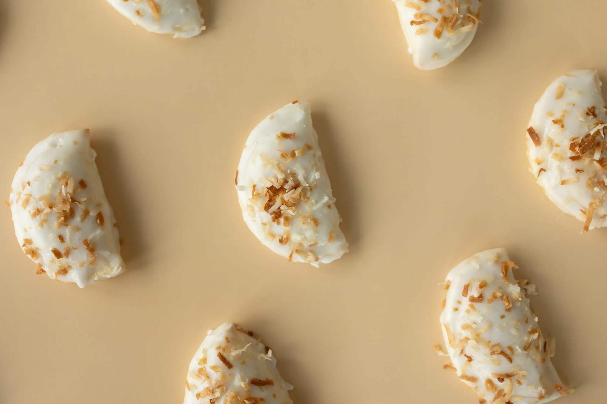 Coconut-topped glazed hand pies scattered in a pattern on a peach background