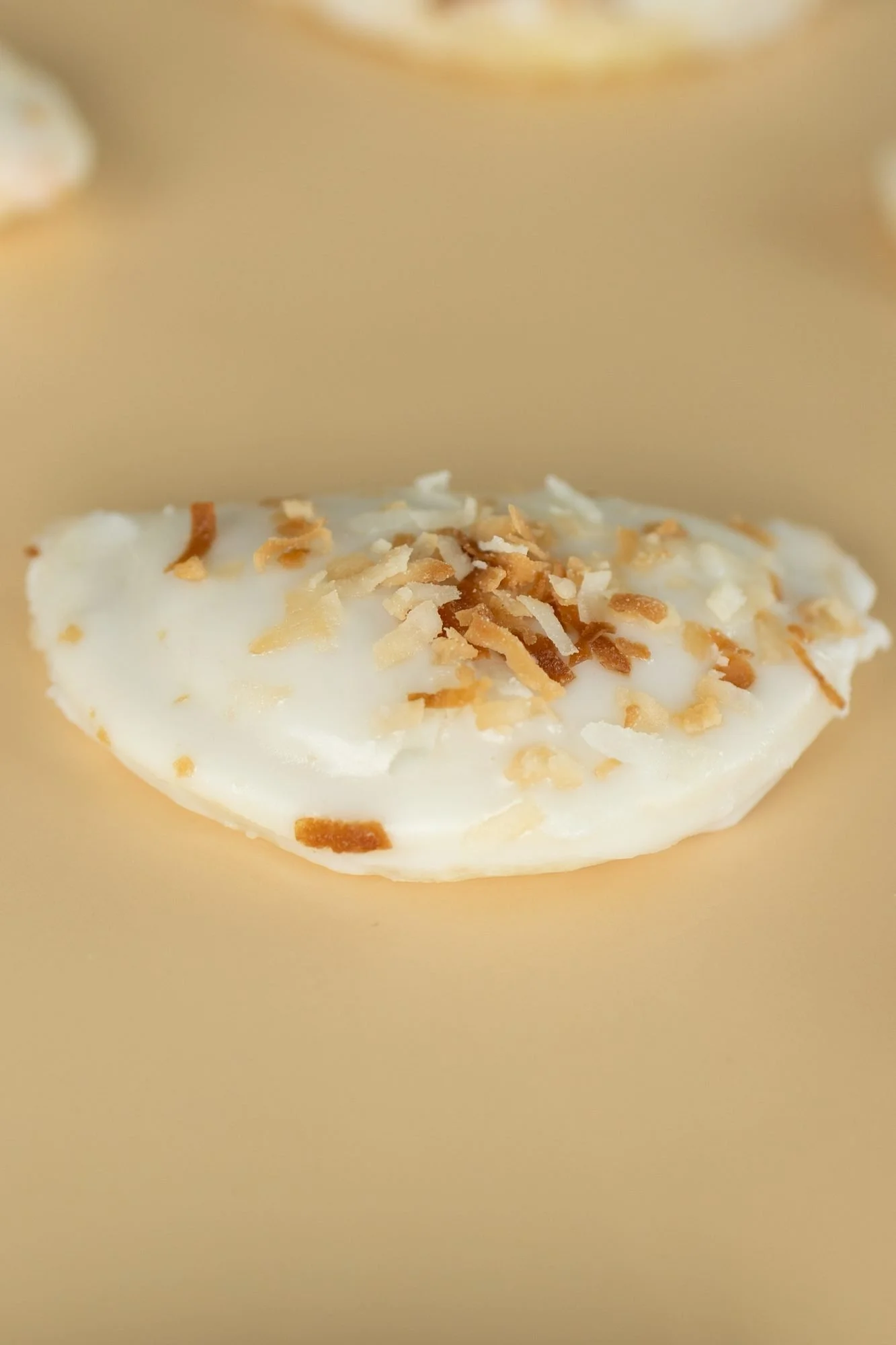 Close view of a white-glazed hand pie topped with toasted coconut on a tan surface