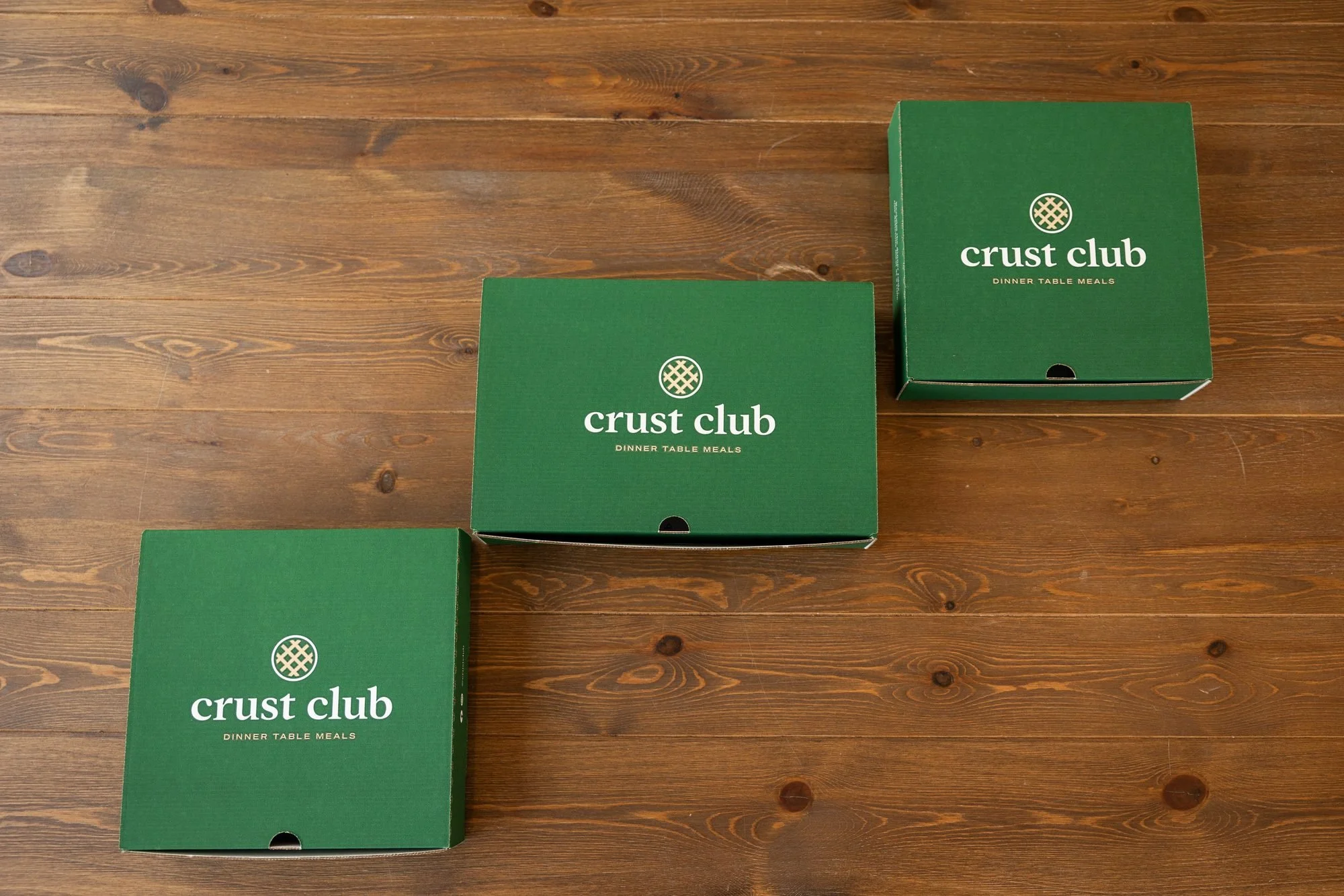 Three green Crust Club boxes arranged on a wooden table