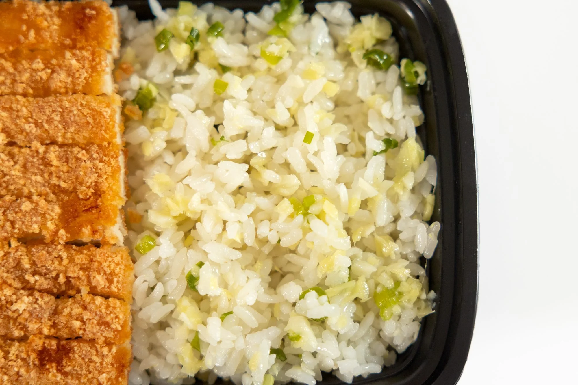 Close view of a breaded cutlet and seasoned rice in a black takeout container