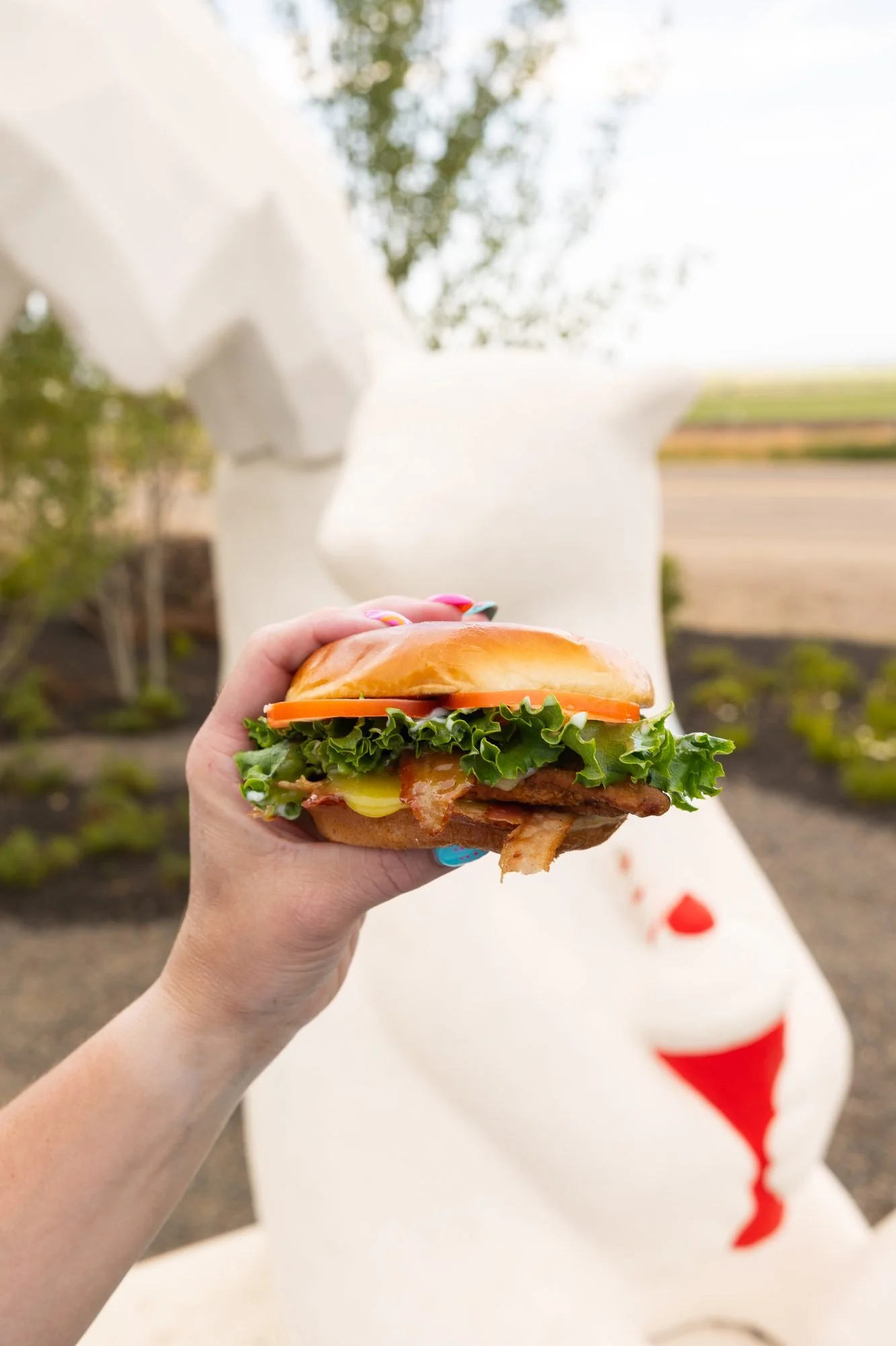 A hand holds a burger in front of a white polar bear statue