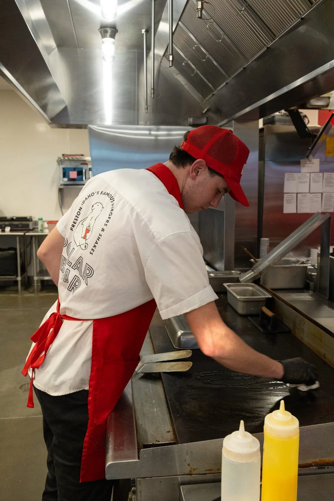 A Polar Bear cook in a red cap and apron works at the flat-top grill in a steel kitchen