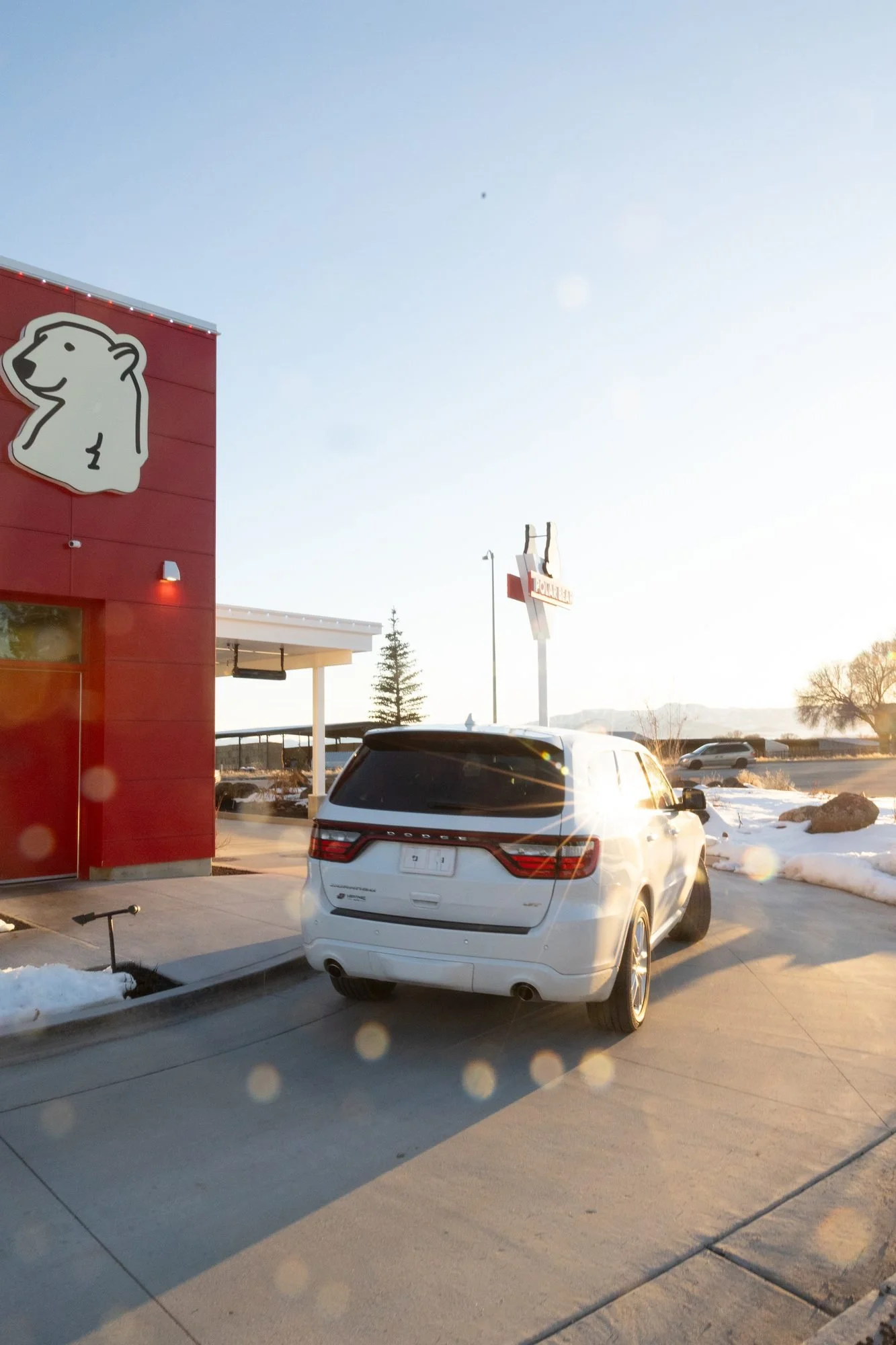A white SUV pulls up to a red Polar Bear building with a polar bear logo on a sunny winter day