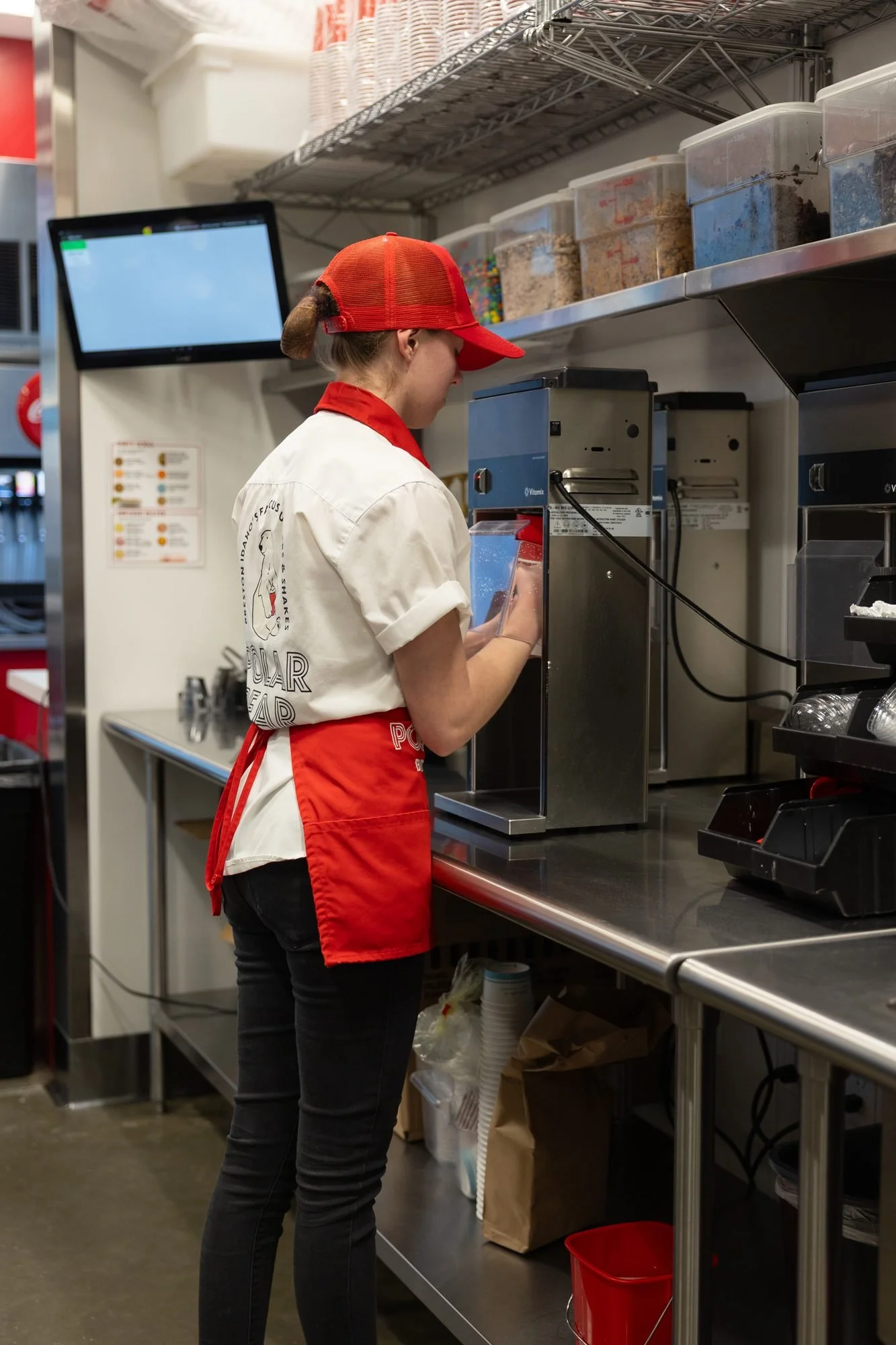 A Polar Bear employee in a red apron works at a shake machine in the kitchen