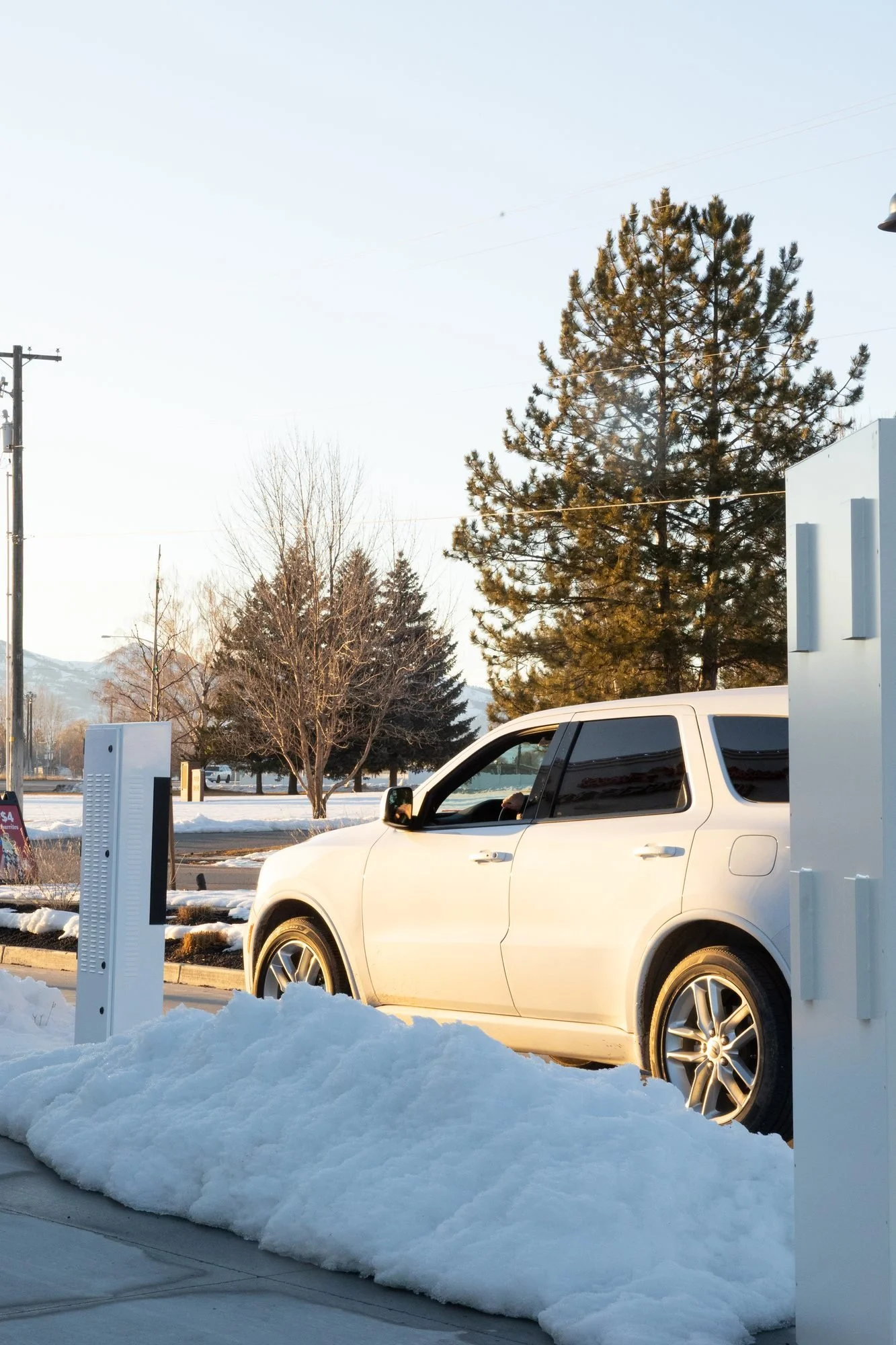 A white SUV in a snowy drive-through lane beside a menu board on a bright winter afternoon