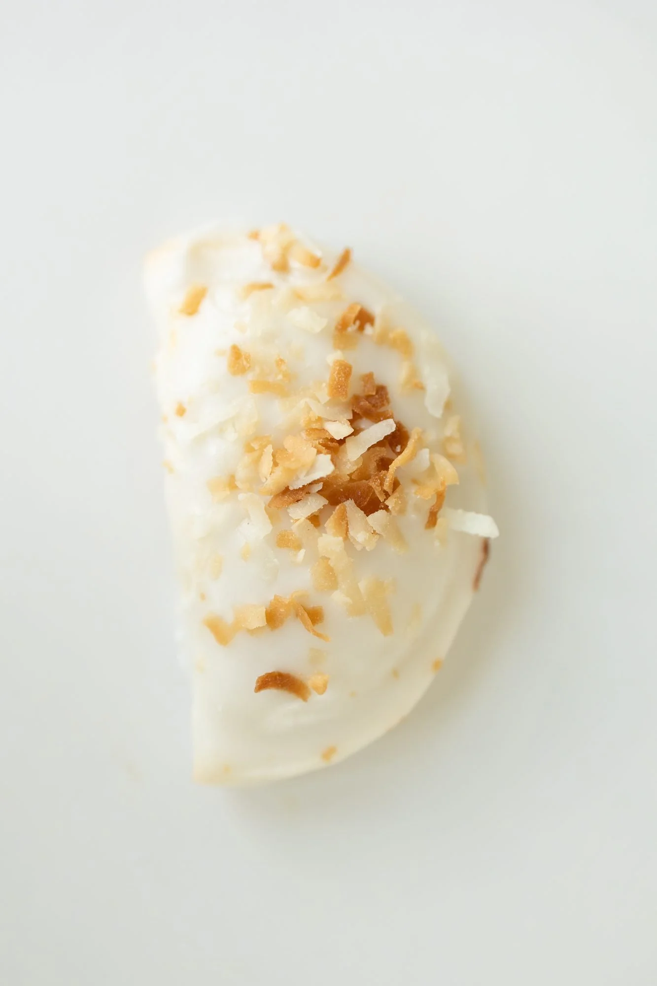 A glazed hand pie with a cluster of toasted coconut on white