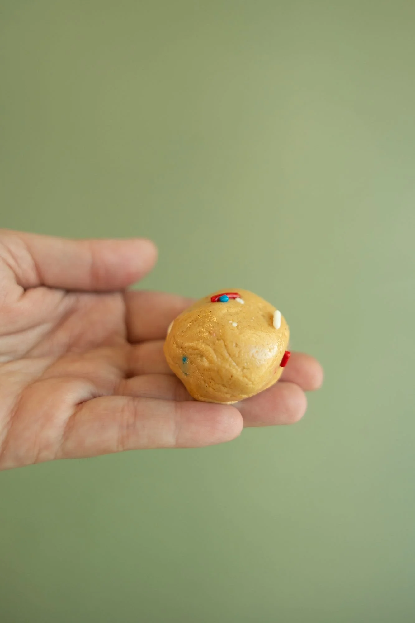 An open palm holds a small cookie dough ball against green