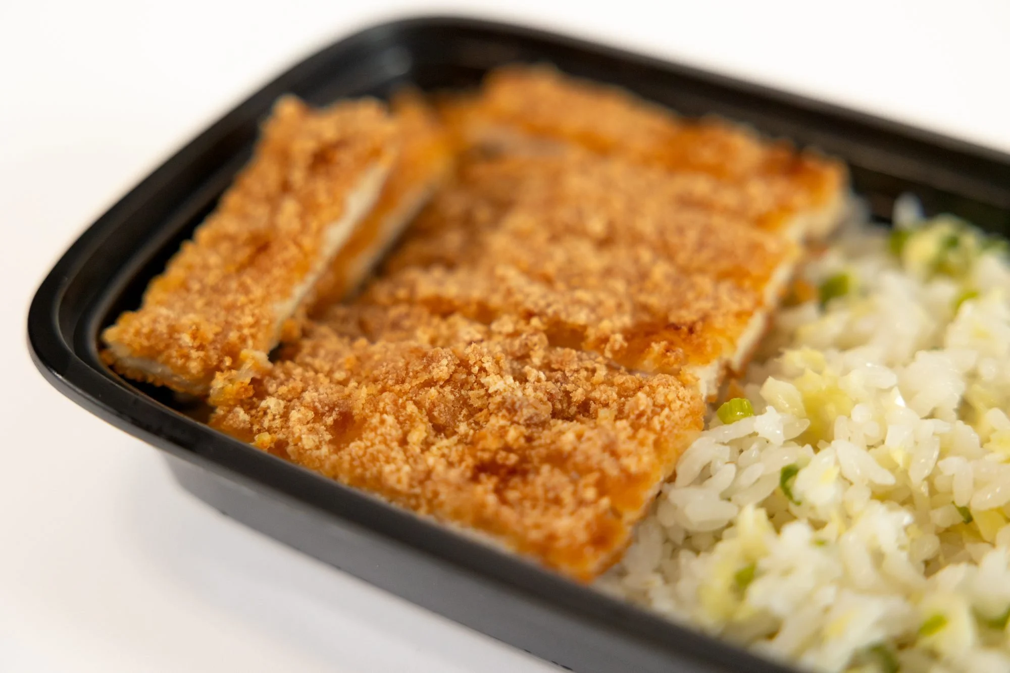 An angled close view of breaded cutlet and seasoned rice in a black container
