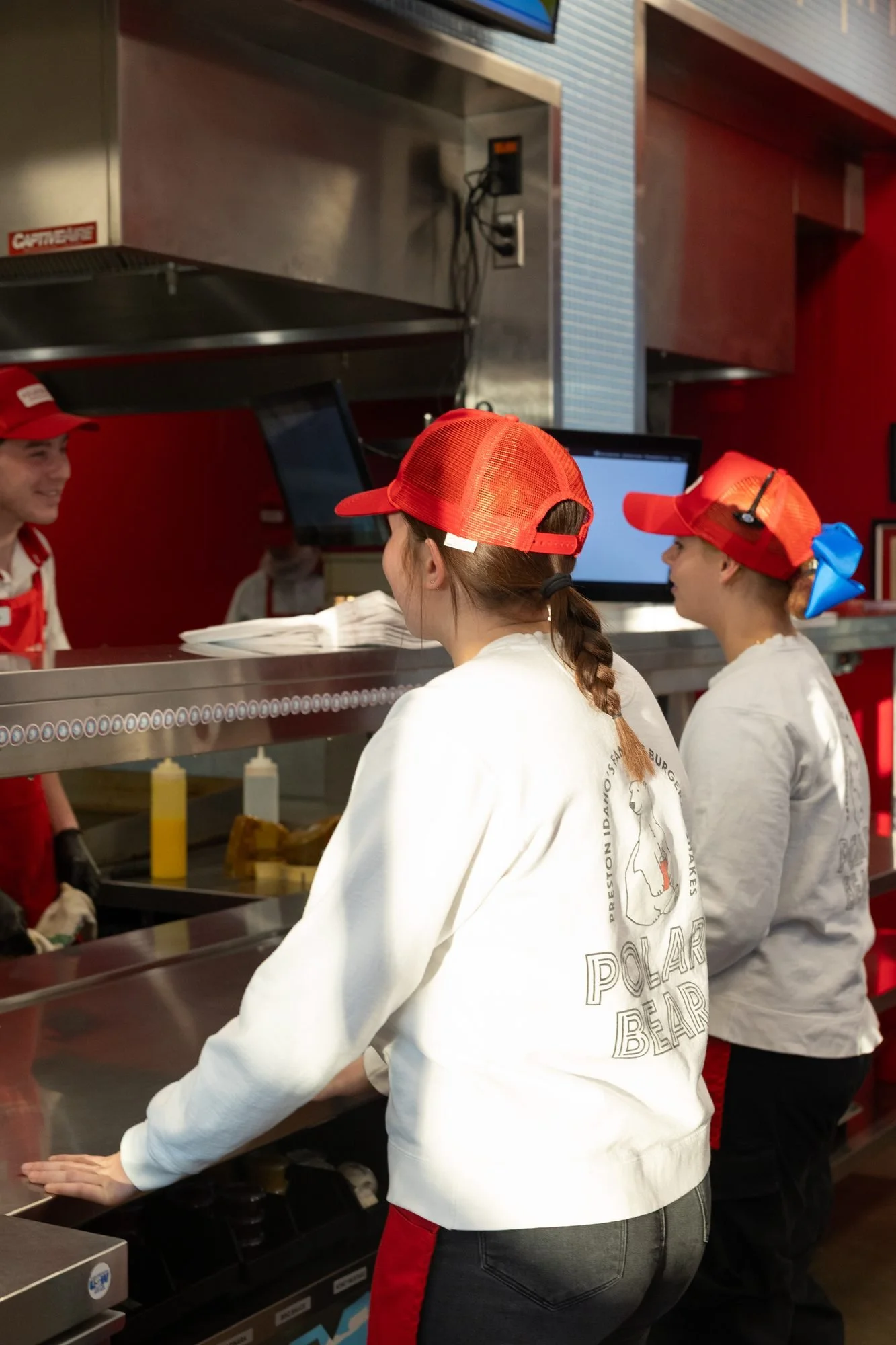 Two Polar Bear employees in red caps work at the kitchen line, seen from behind
