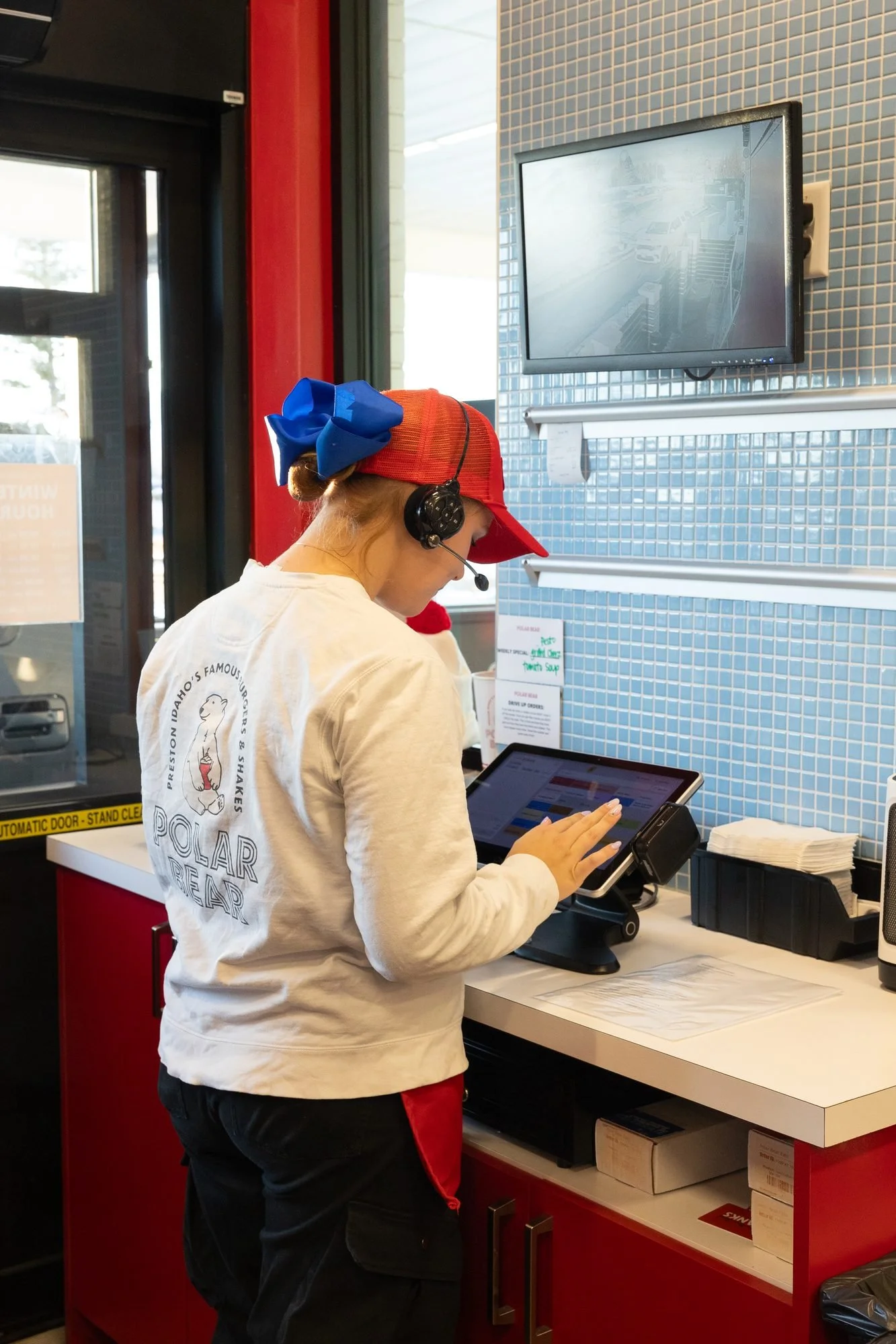 A Polar Bear employee with a headset takes an order on a tablet at the drive-through window
