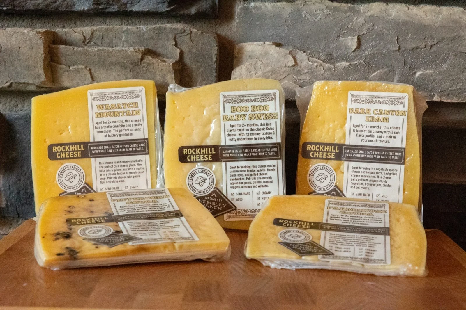 Five wrapped wedges of cheese with printed labels lined up on a wooden board