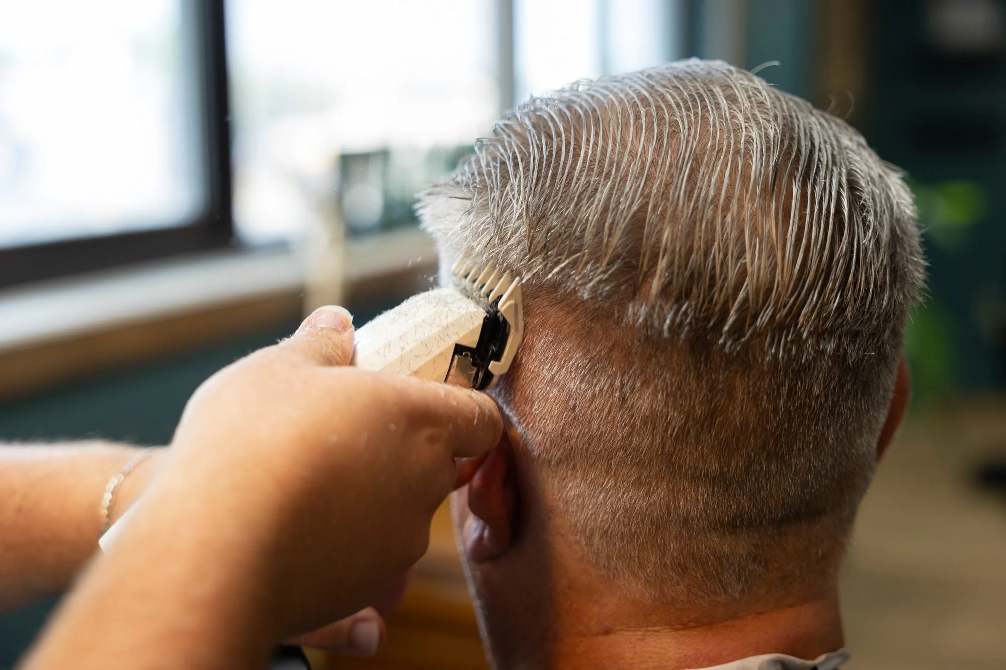 Close view of a barber's hands trimming the back of a client's gray hair with clippers