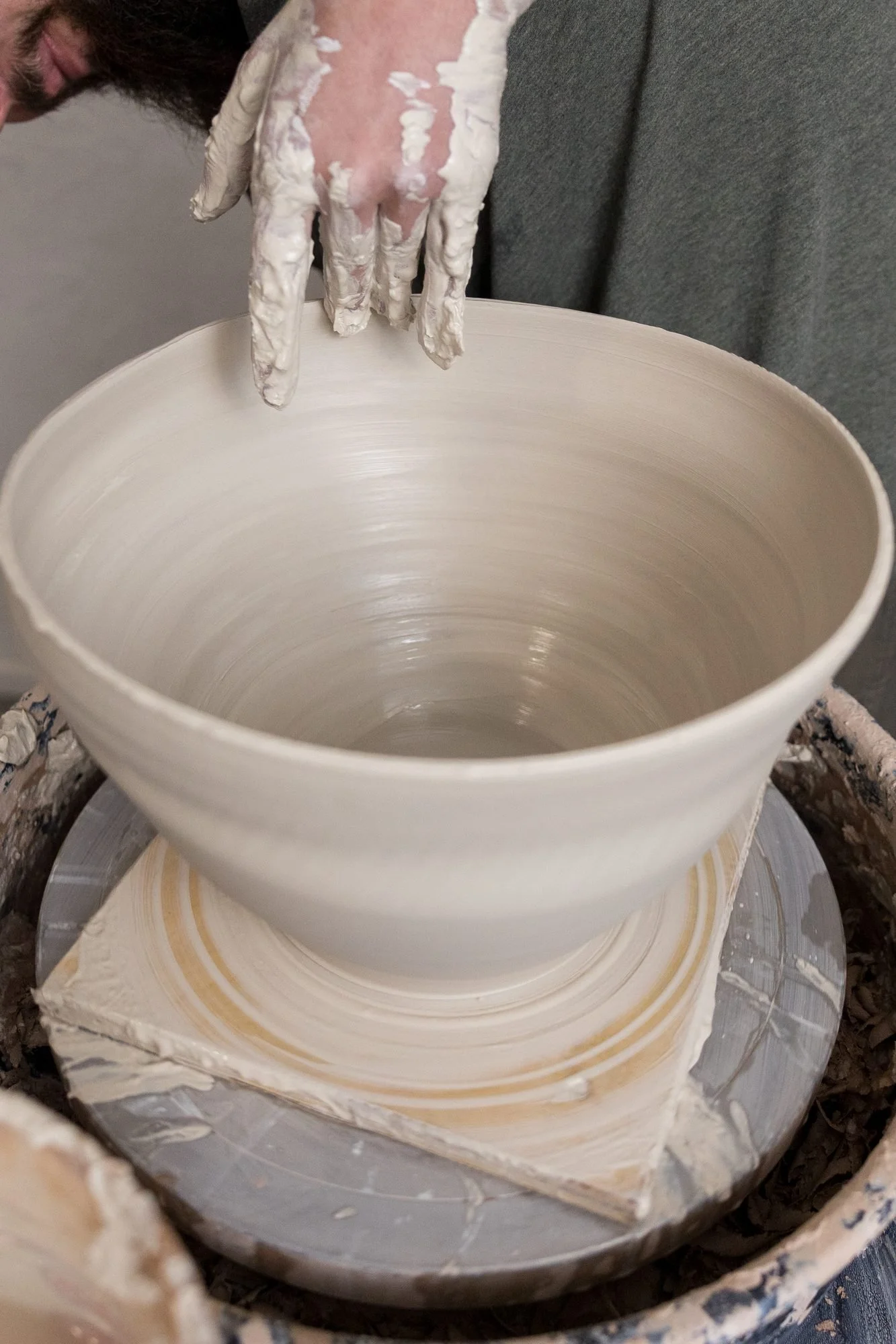 A clay-covered hand smoothing the inside of a wide bowl on a pottery wheel