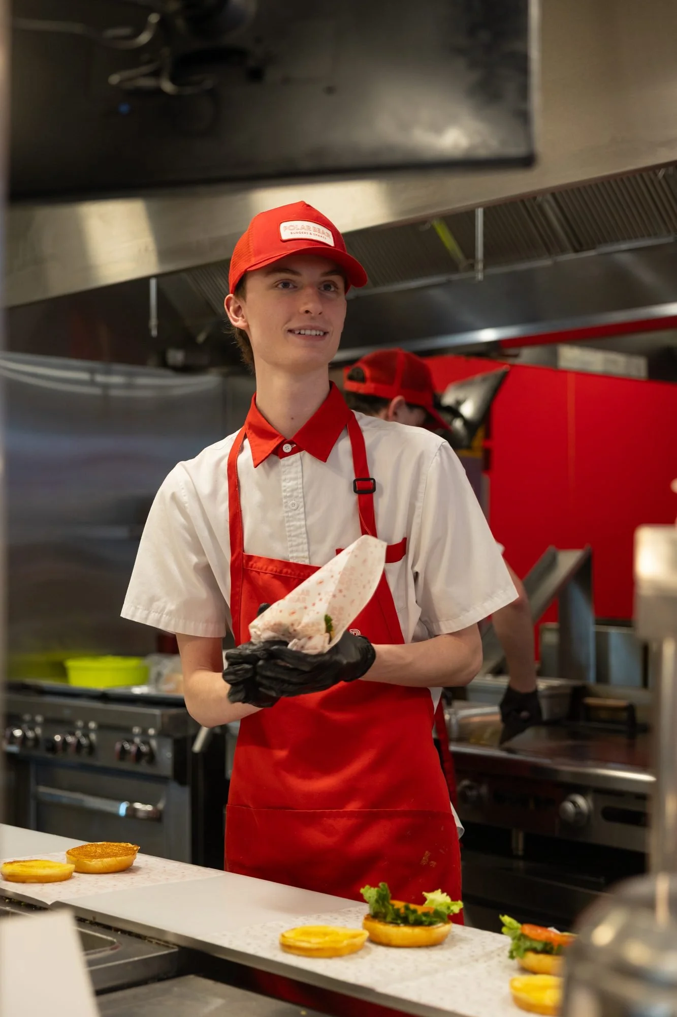 A young Polar Bear employee in a red cap and apron smiling in the kitchen