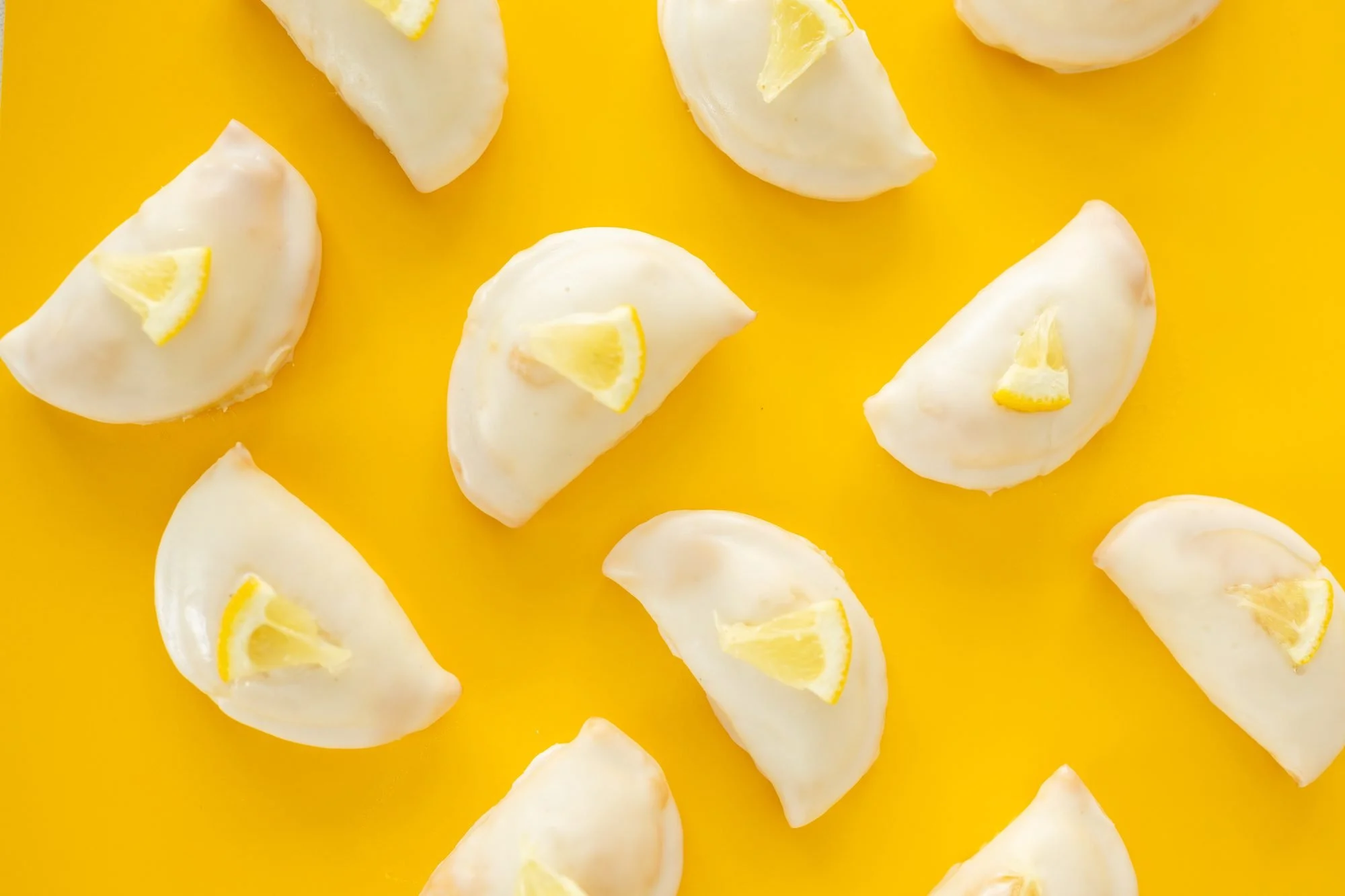 Glazed hand pies topped with lemon wedges scattered across a bright yellow background