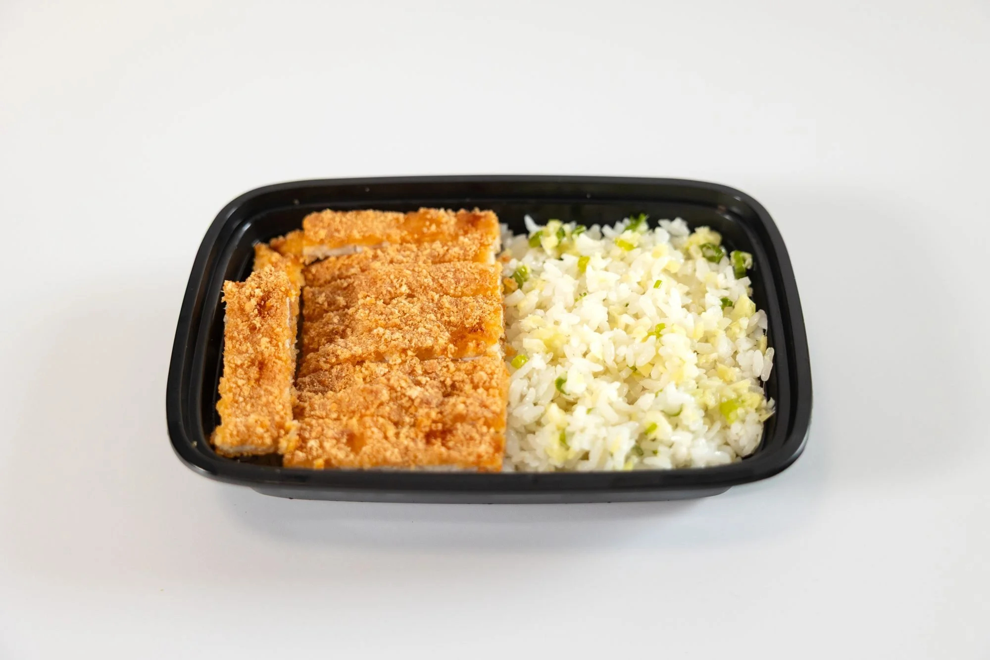 A black takeout container with breaded cutlet strips and rice on a white background