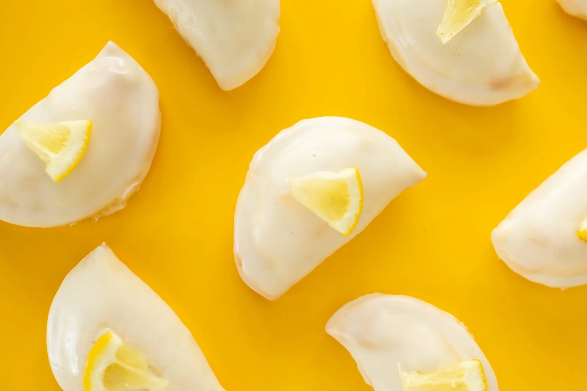 Glazed hand pies topped with lemon wedges arranged across a bright yellow surface
