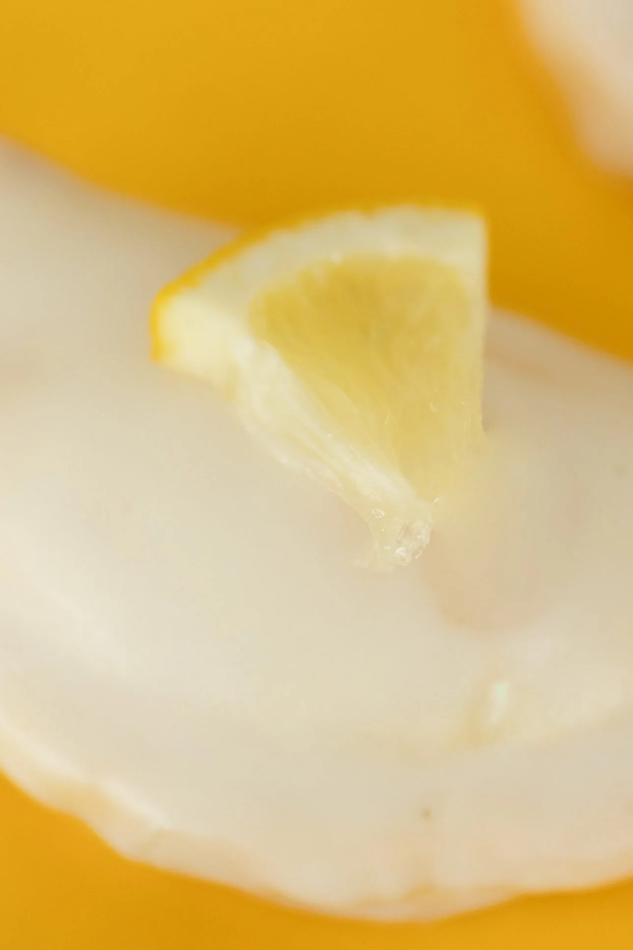 Close view of a glazed hand pie topped with a lemon wedge on a yellow background