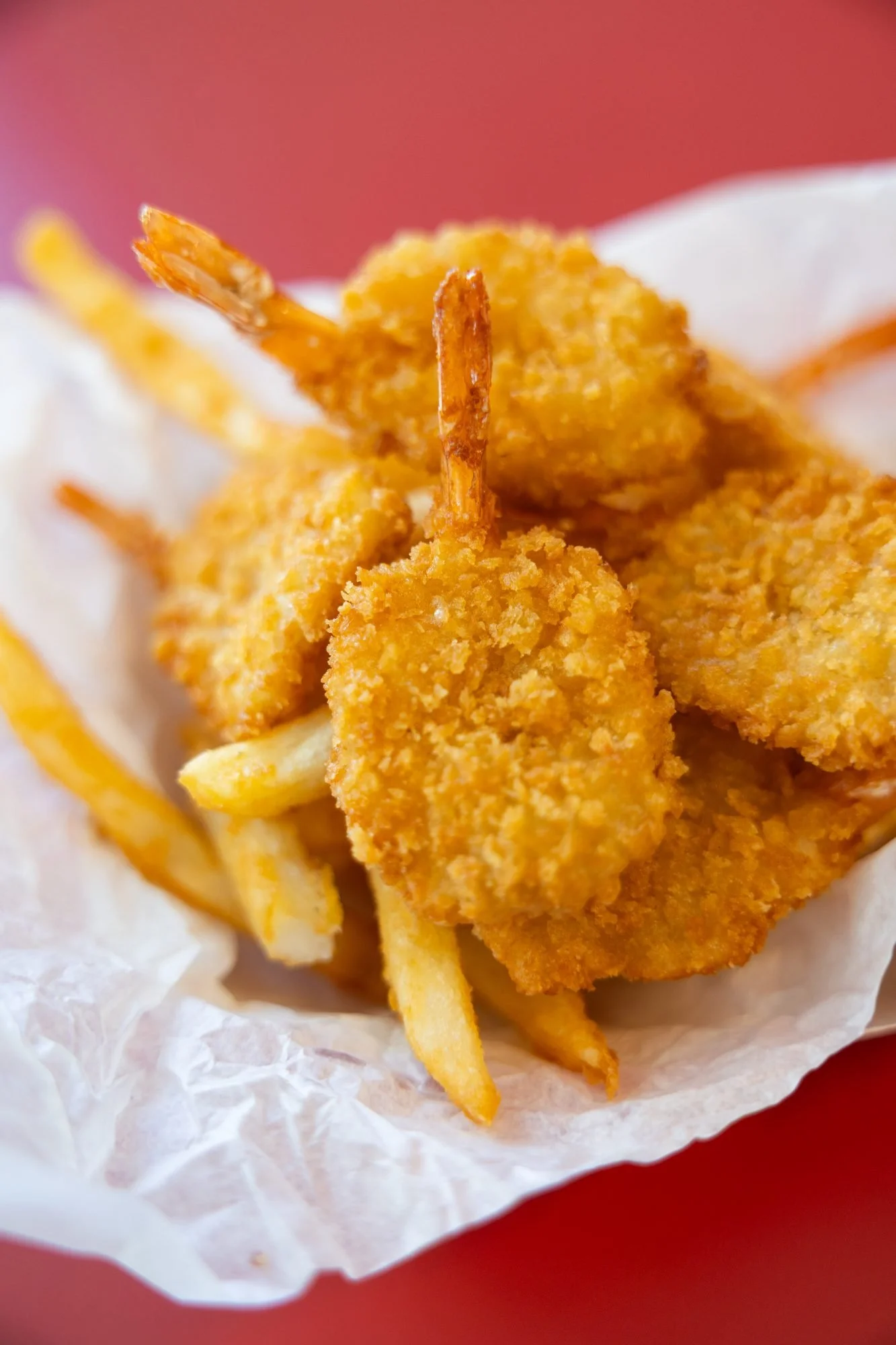 Breaded shrimp and fries in a paper-lined basket on a red background