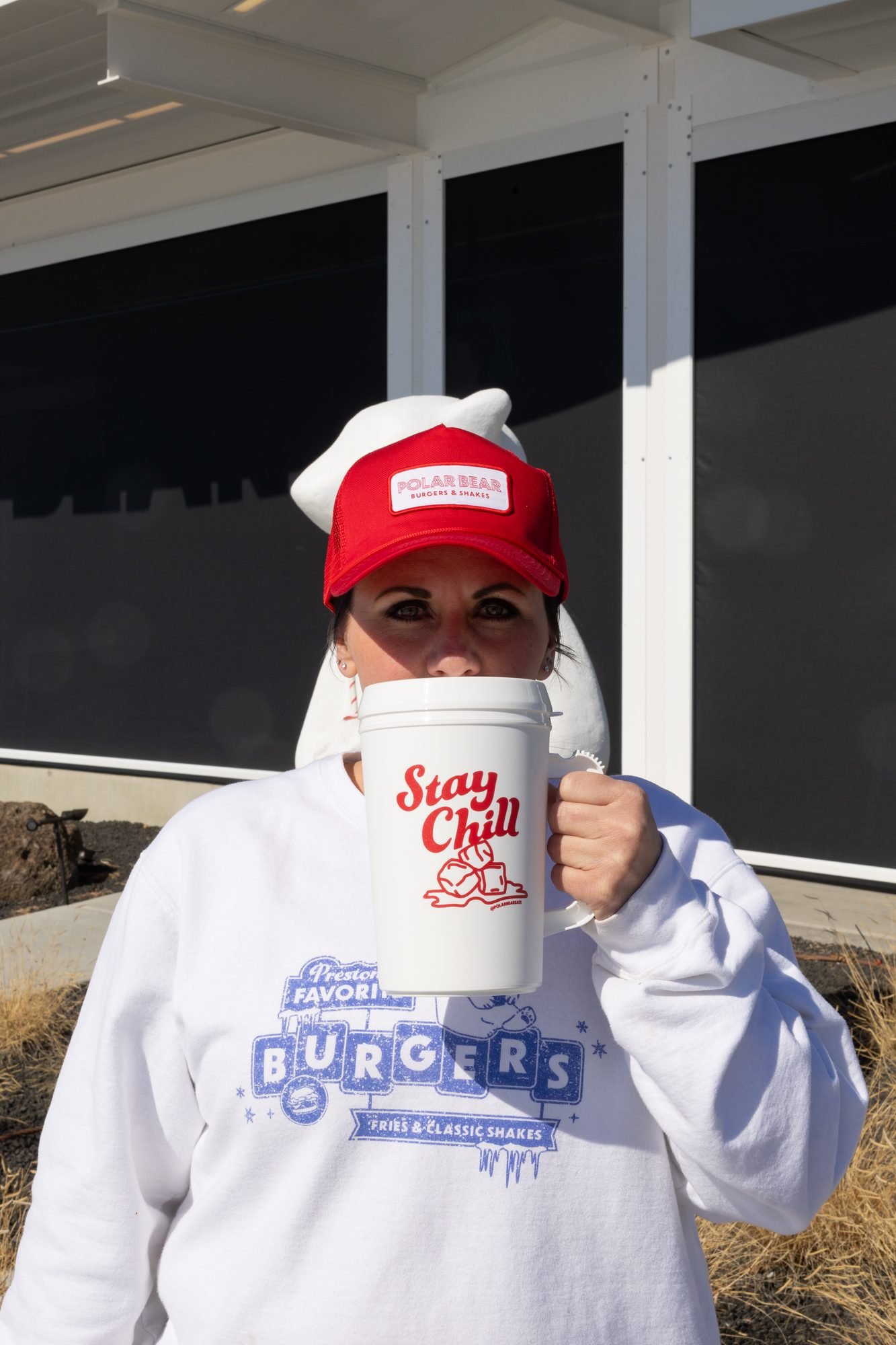 A woman in a red Polar Bear cap holding a Stay Chill mug in front of the building