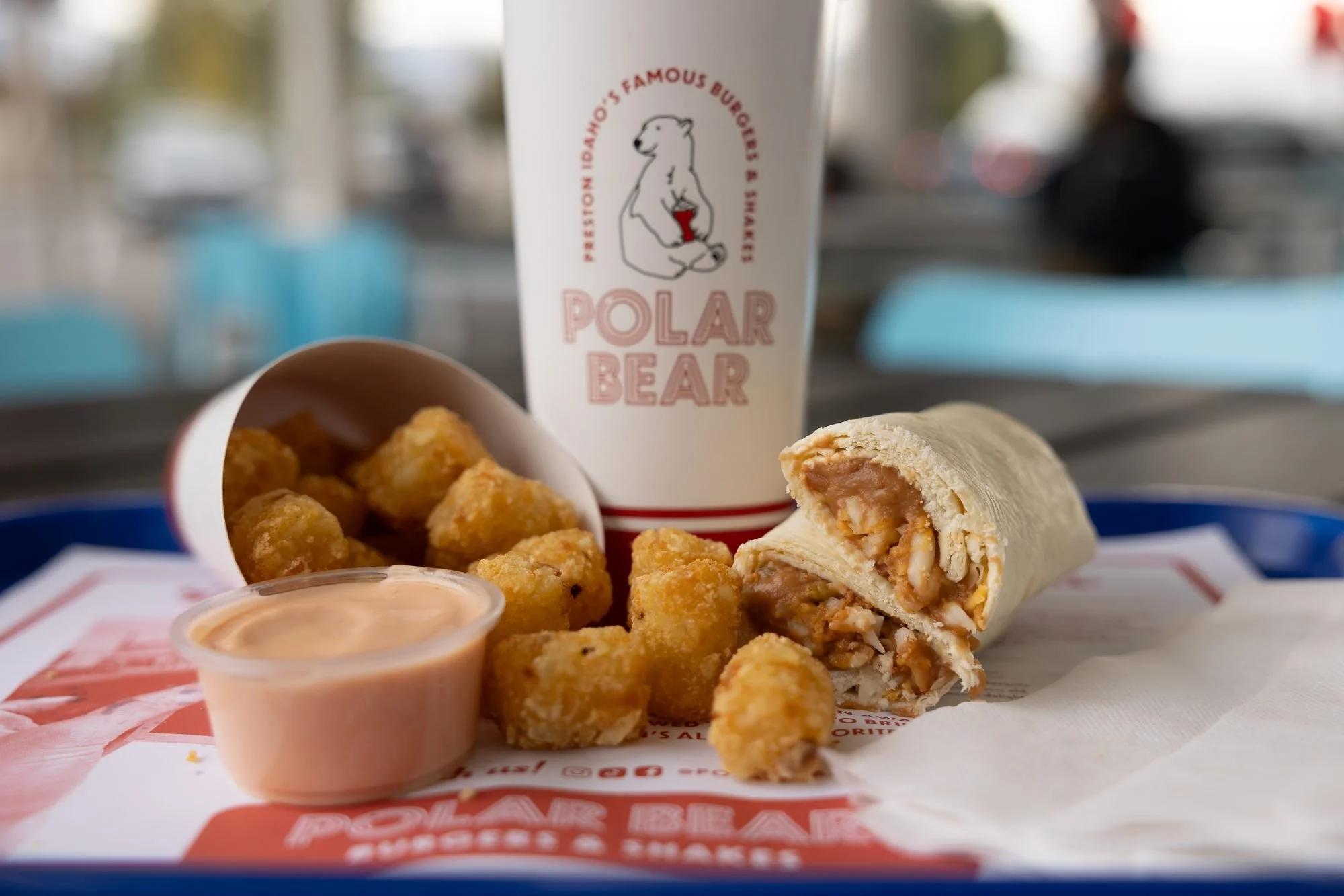 A Polar Bear drink, tater tots, sauce and a wrap on a tray on a table