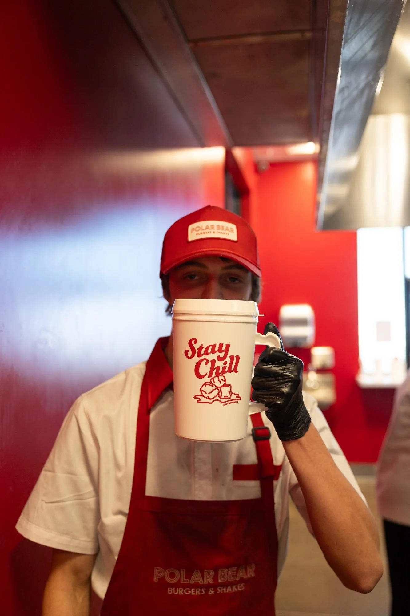 A Polar Bear crew member in an apron holding a Stay Chill mug in the kitchen