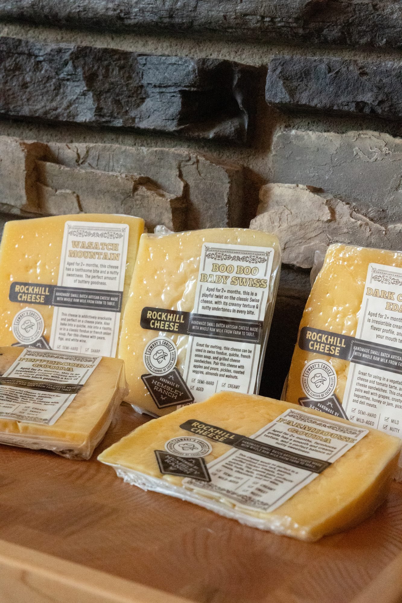 Labeled blocks of Rockhill cheese stacked on a wooden board in front of a stone wall